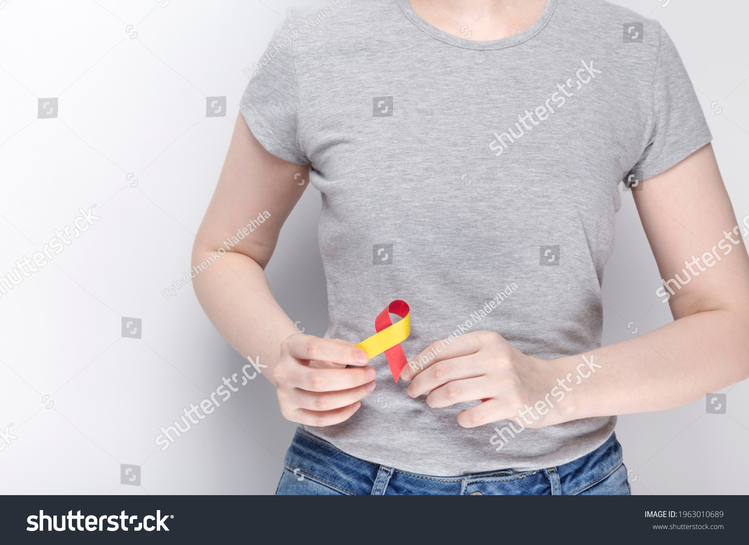 World Hepatitis Day Concept. Girl in gray T-shirt holding red-yellow ribbon area liveras symbol of awareness. Gray background. Copy space