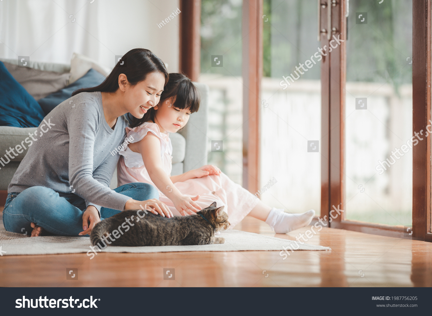 Happy Asian family mother and daughter palying with cat at home in living room. Focused on mother