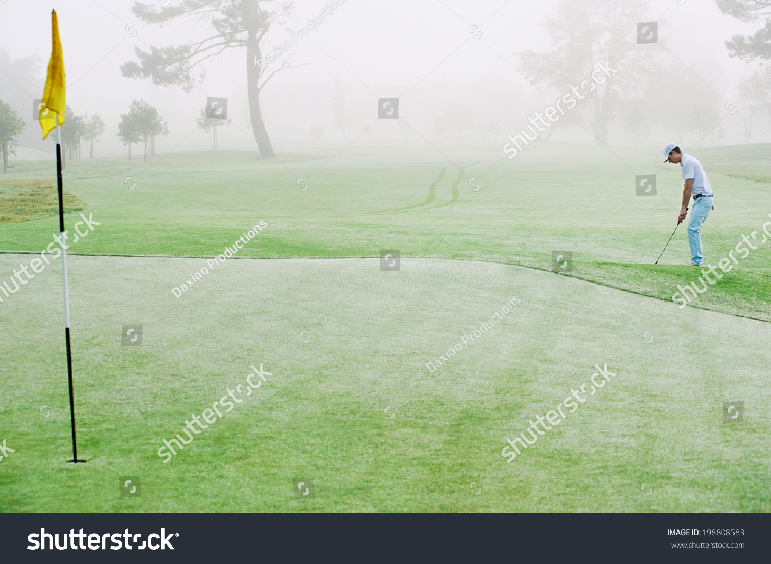 Golfer chipping onto the green at sunrise on the golf course in misty conditions
