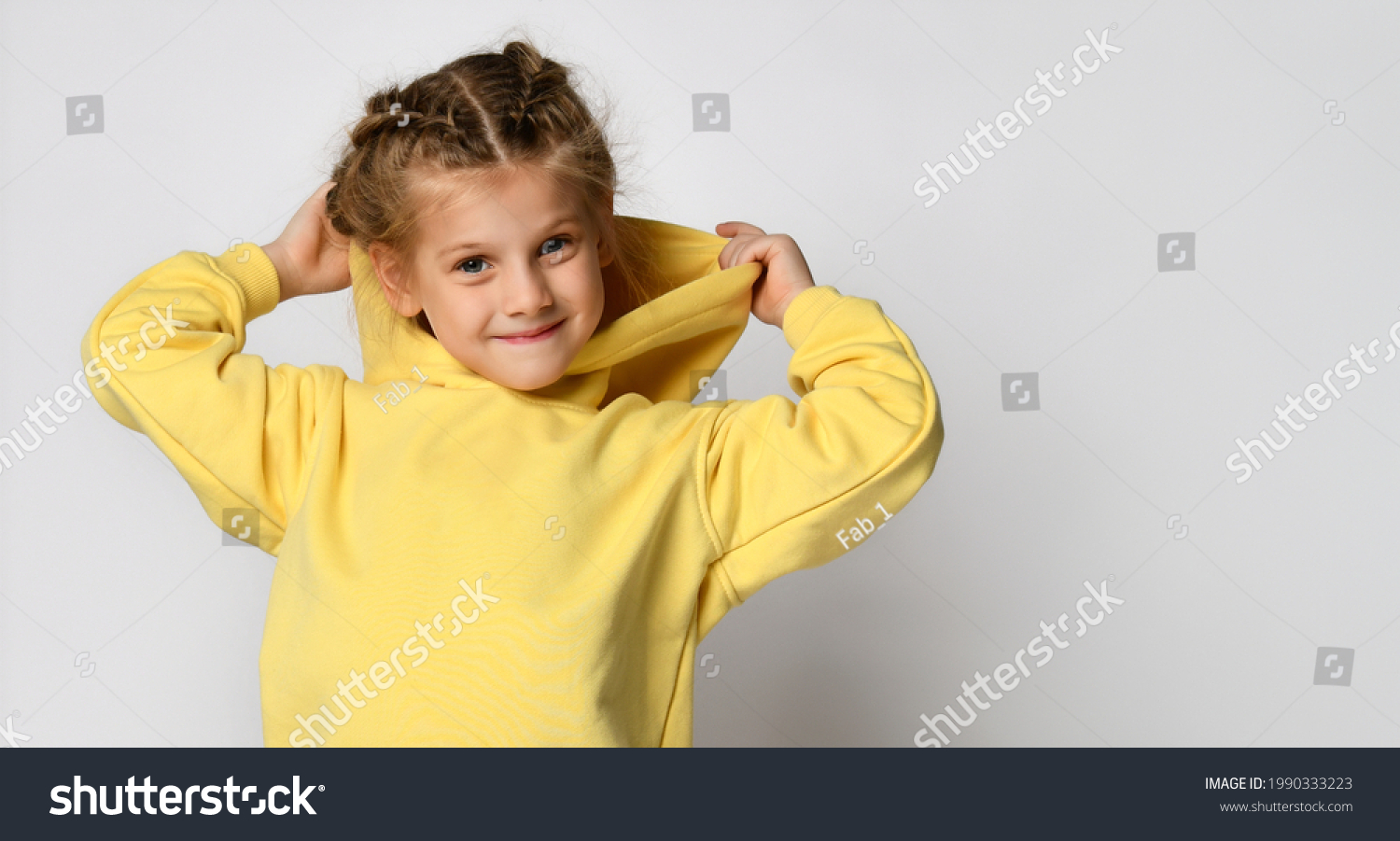 Portrait of a joyful active little girl wearing a hood on a white background. Happy cute child in a yellow sports hoodie white background. Sportswear advertising concept. Banner.