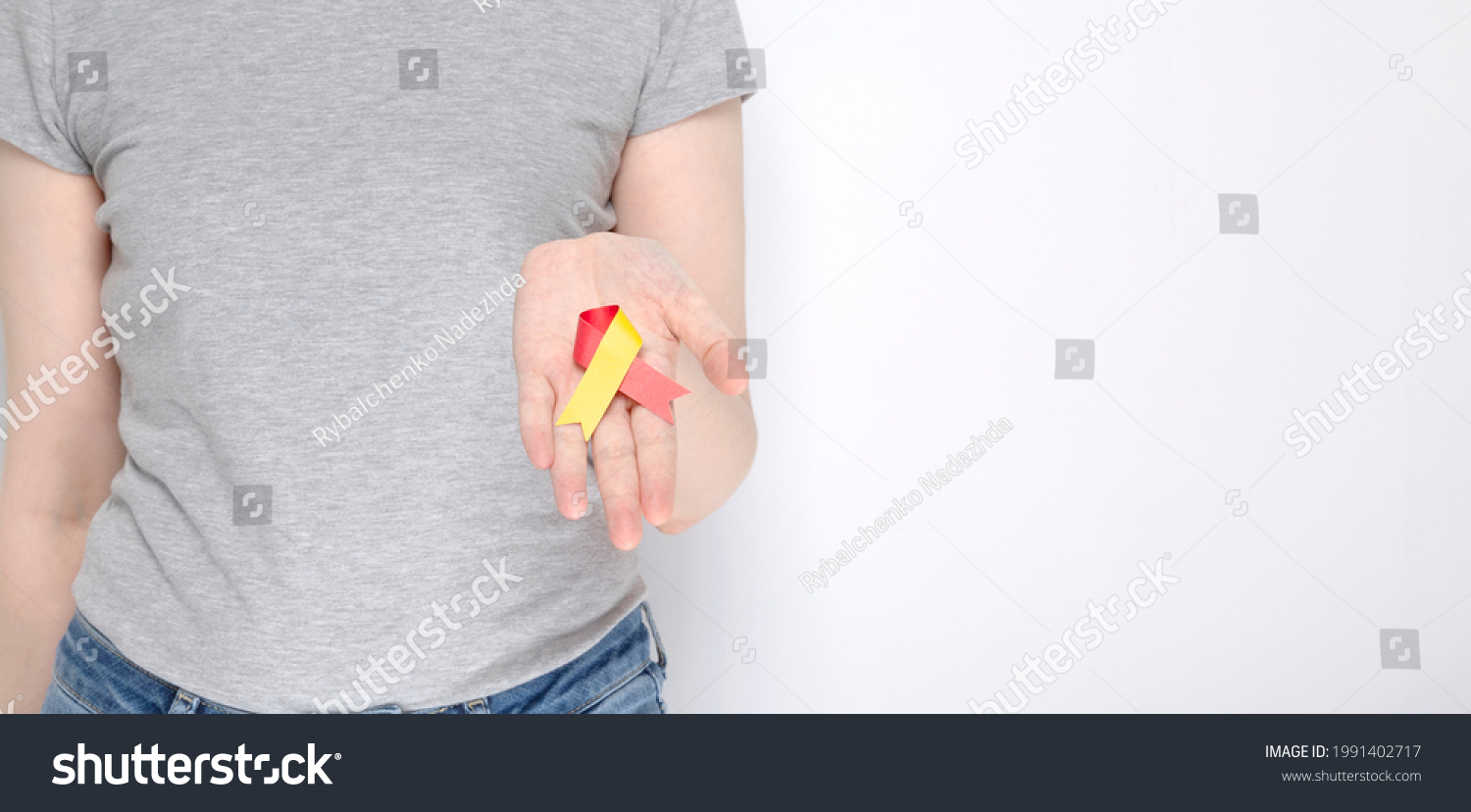 World Hepatitis Day concept. Girl in gray T-shirt holds in her hand awareness symbol red-yellow ribbon. Gray background. Copy space