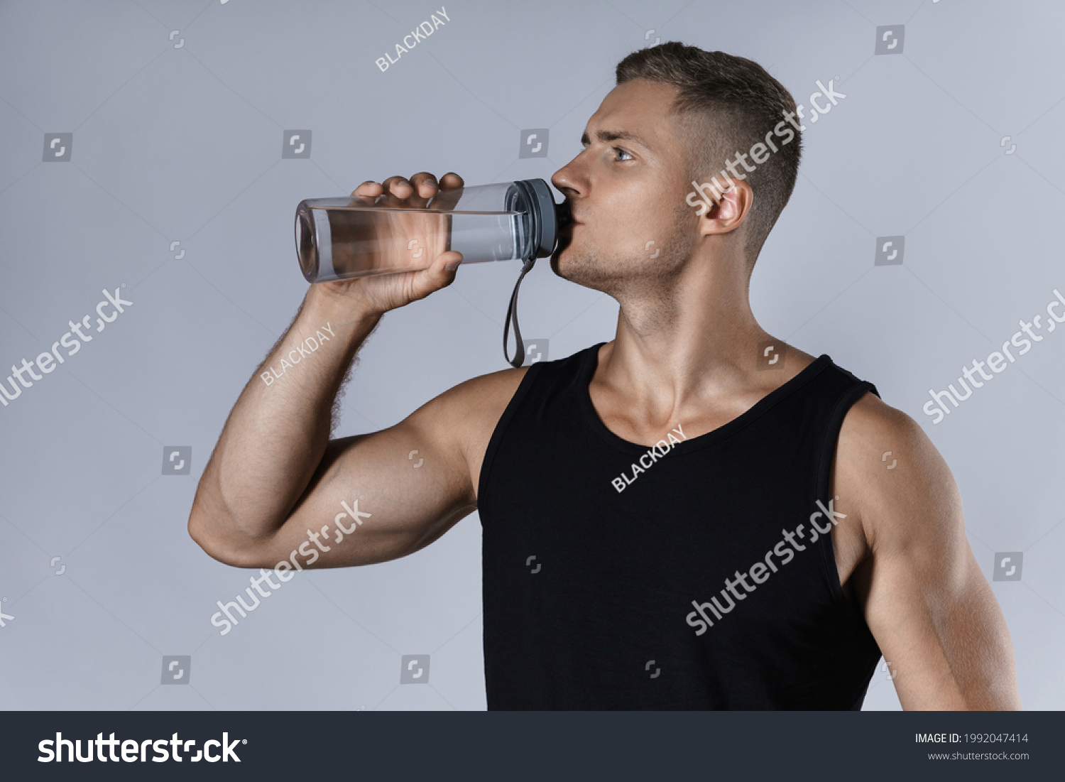 Young and handsome athletic man drinking water against gray background