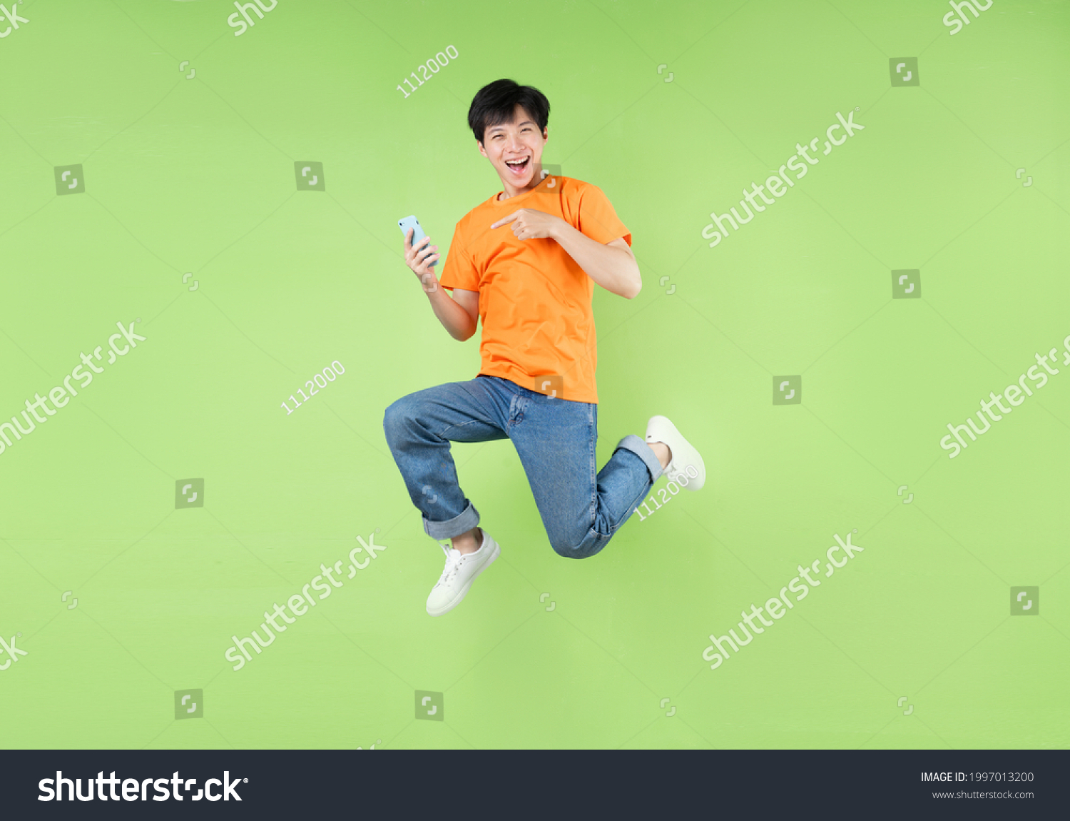 Asian man jumping and holding smartphone   isolated on green