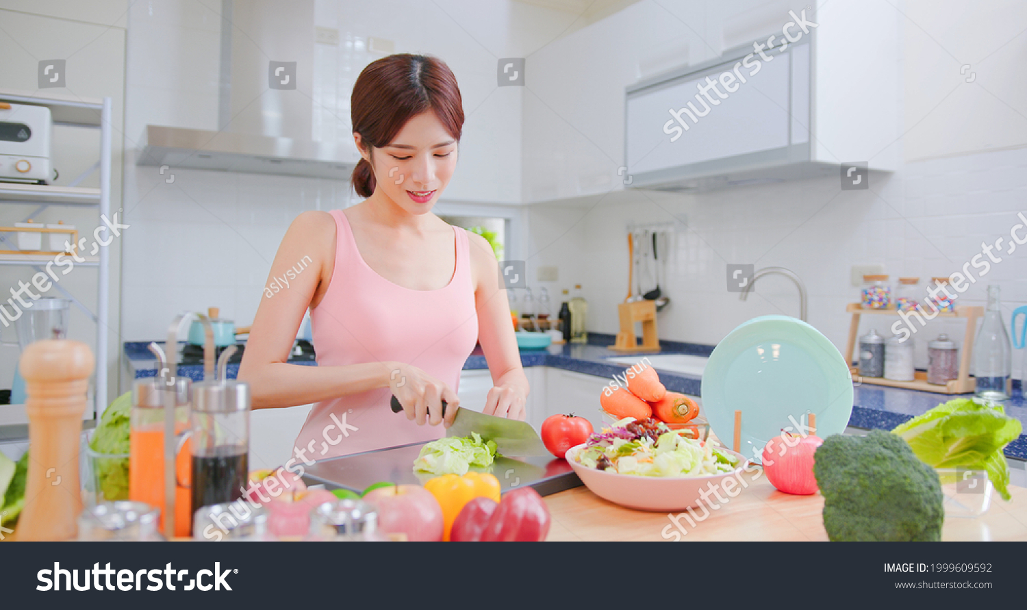 Healthy asian woman making a salad in light white interior style kitchen at home