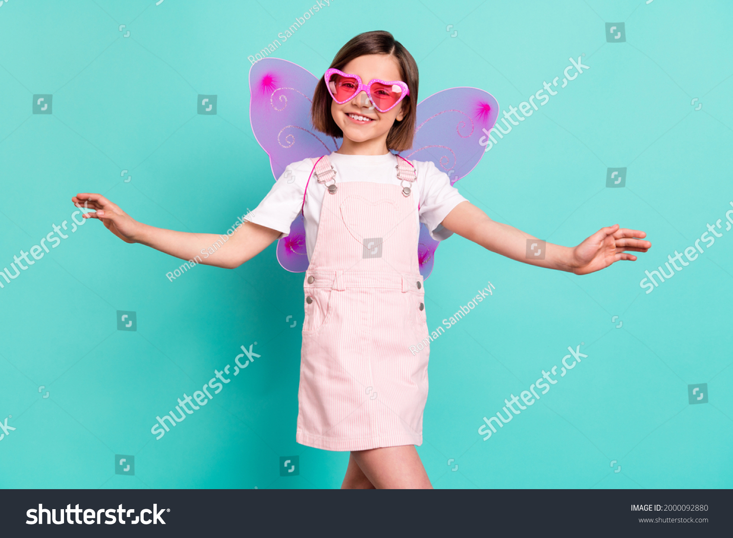 Photo of adorable cute school girl wear pink overall glasses wings smiling dancing isolated teal color background