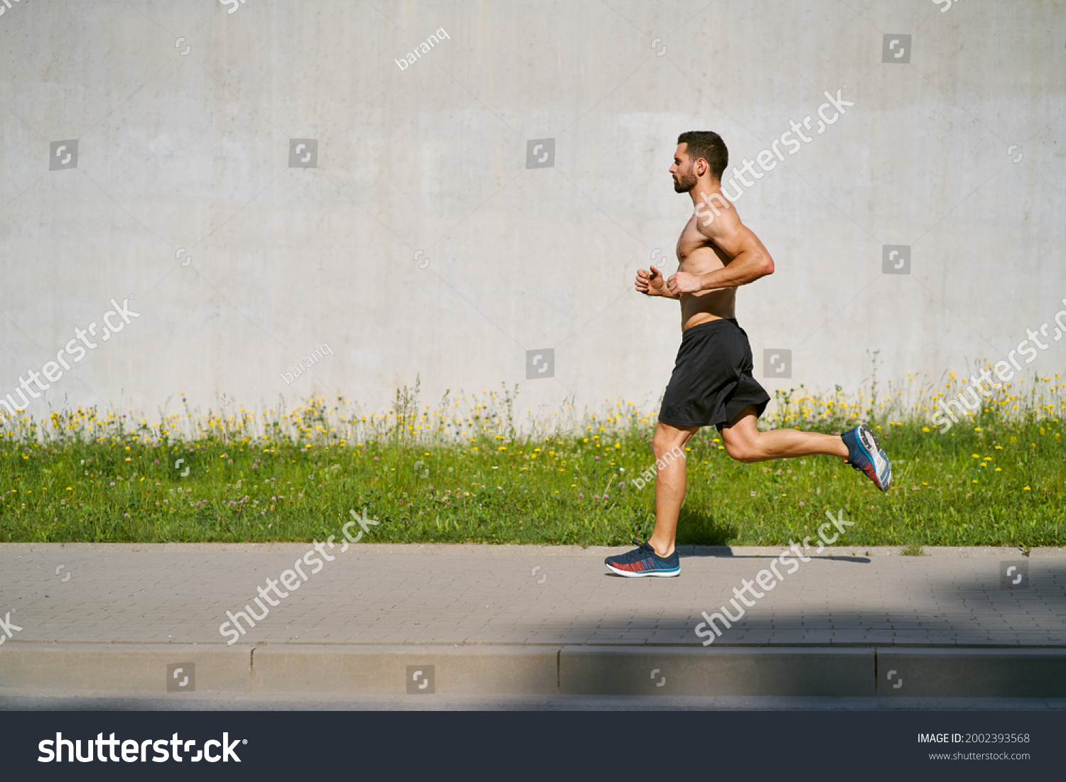 Athletic man running on the sidewalk shirtless during sunny summer ...