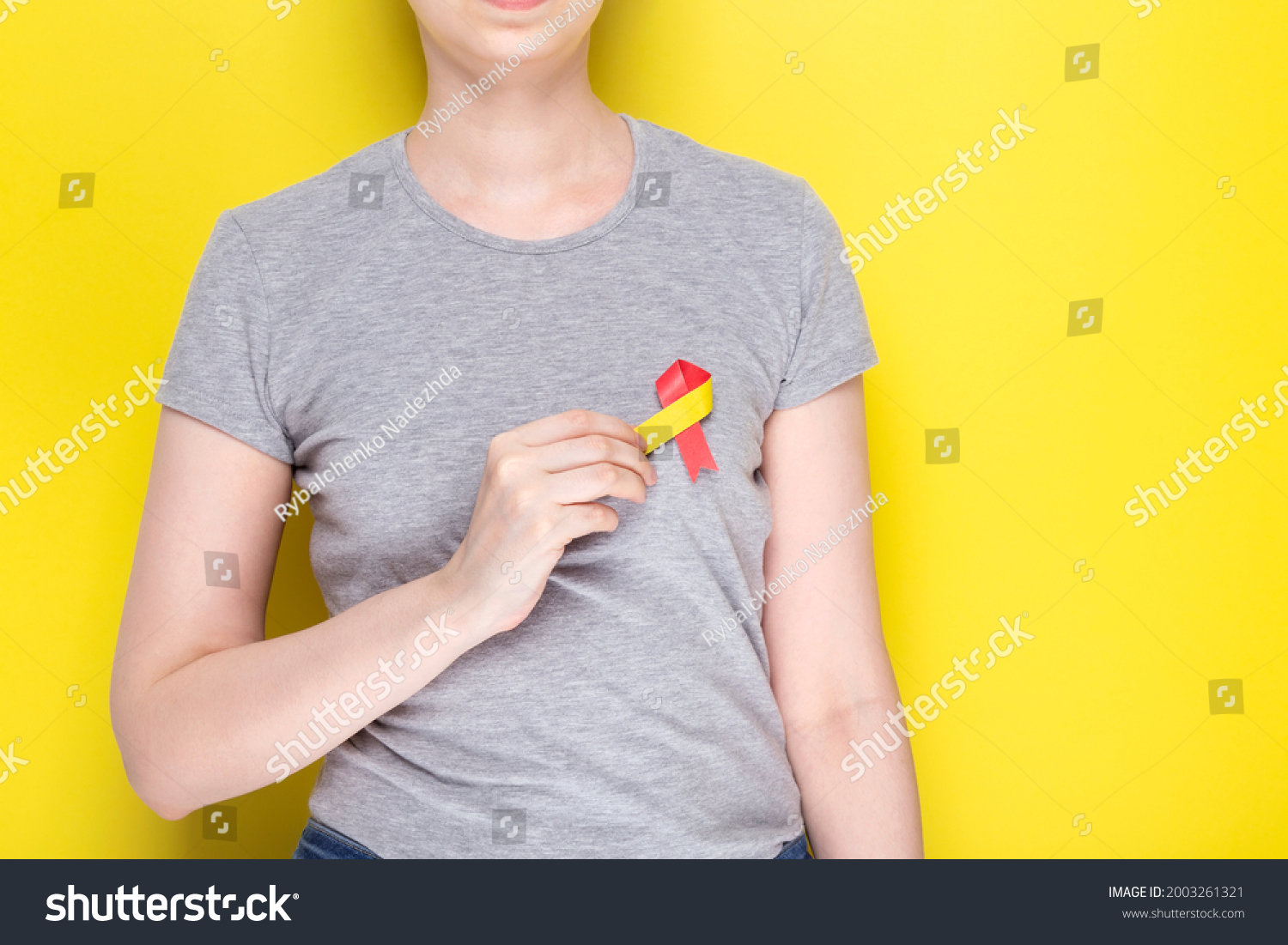 World Hepatitis Day concept. Girl in gray T-shirt holds in her hand awareness symbol red-yellow ribbon. Yellow background. Copy space