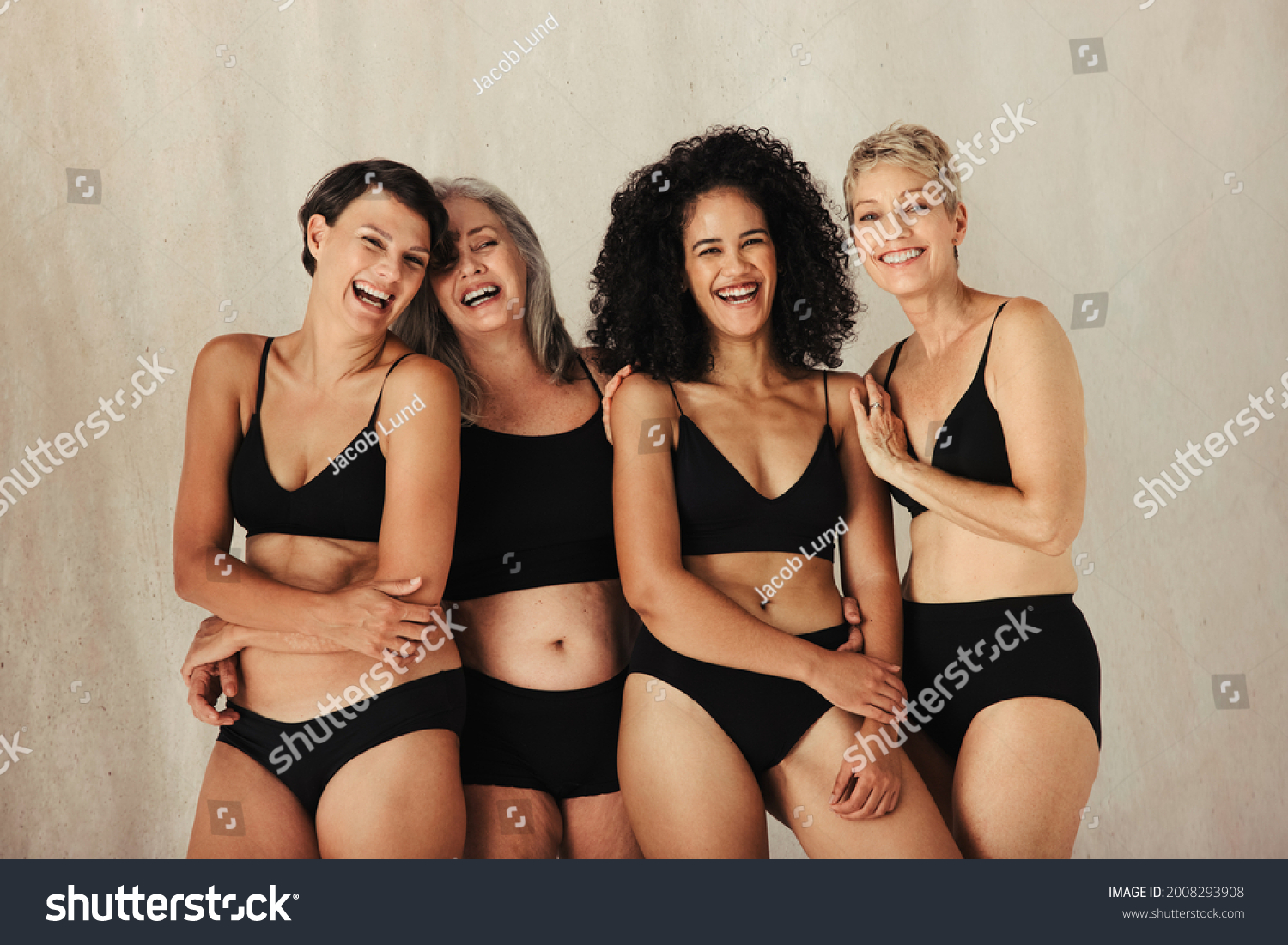 Happy women of different ages embracing their natural bodies. Four women in black underwear smiling and embracing each other. Body positive women standing together against a studio background.
