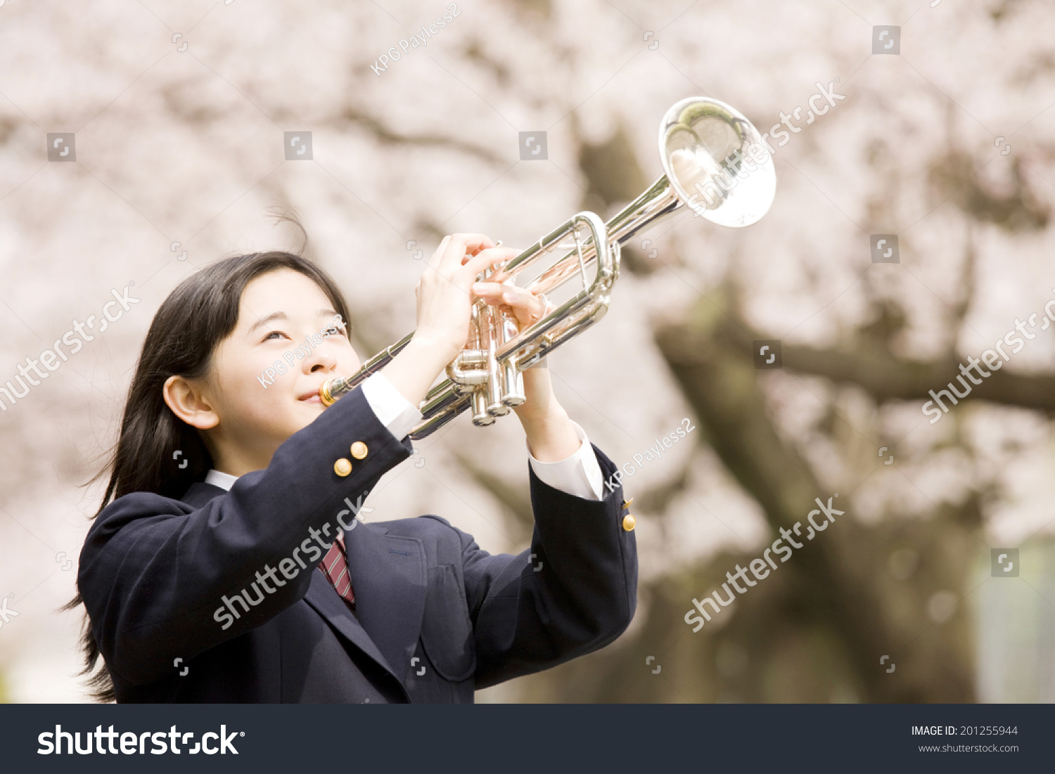 A middle school girl playing a trumpet under cherry blossoms