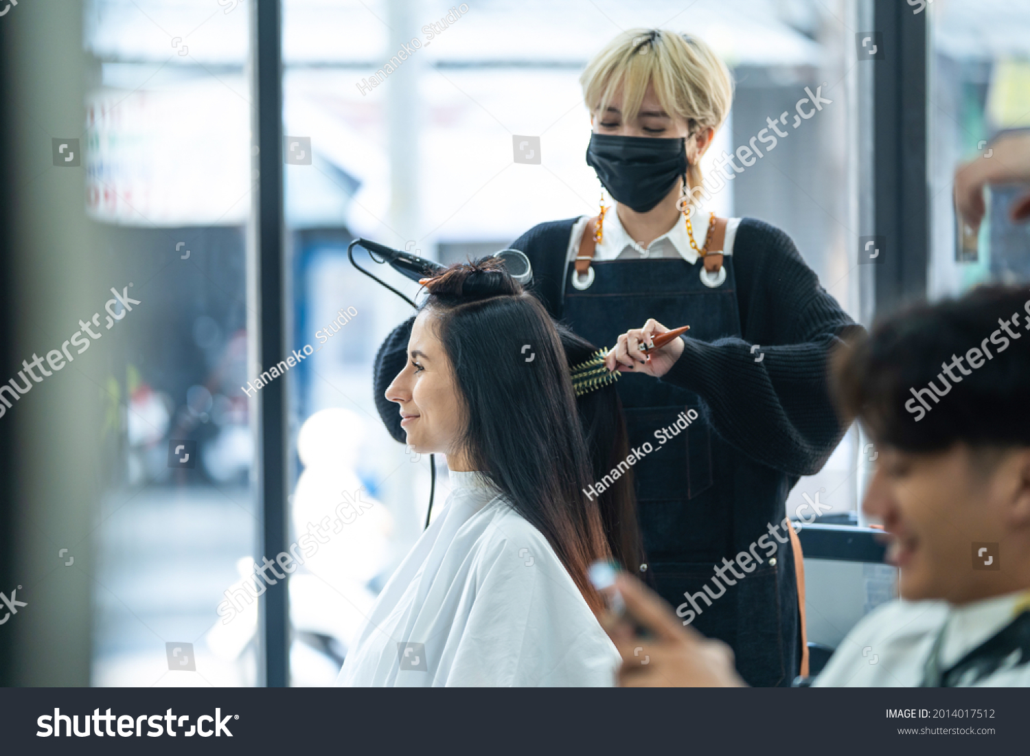 Asian stylist use curling iron make curly to customer's hair in salon. Caucasian beautiful girl with happy face enjoy hairstyle treatment service from Professional hairdresser in beauty barber shop.