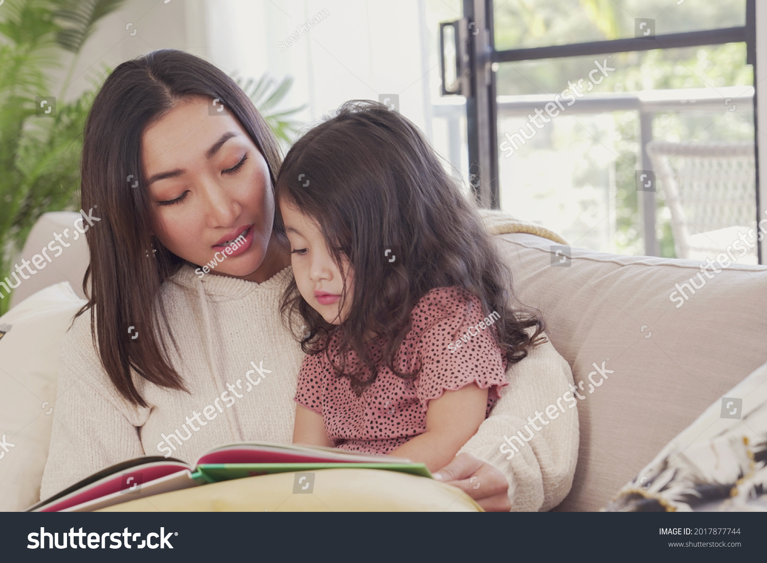 Asian mother read book to her mixed daughter girl at home spending family quality time together homeschooling education concept