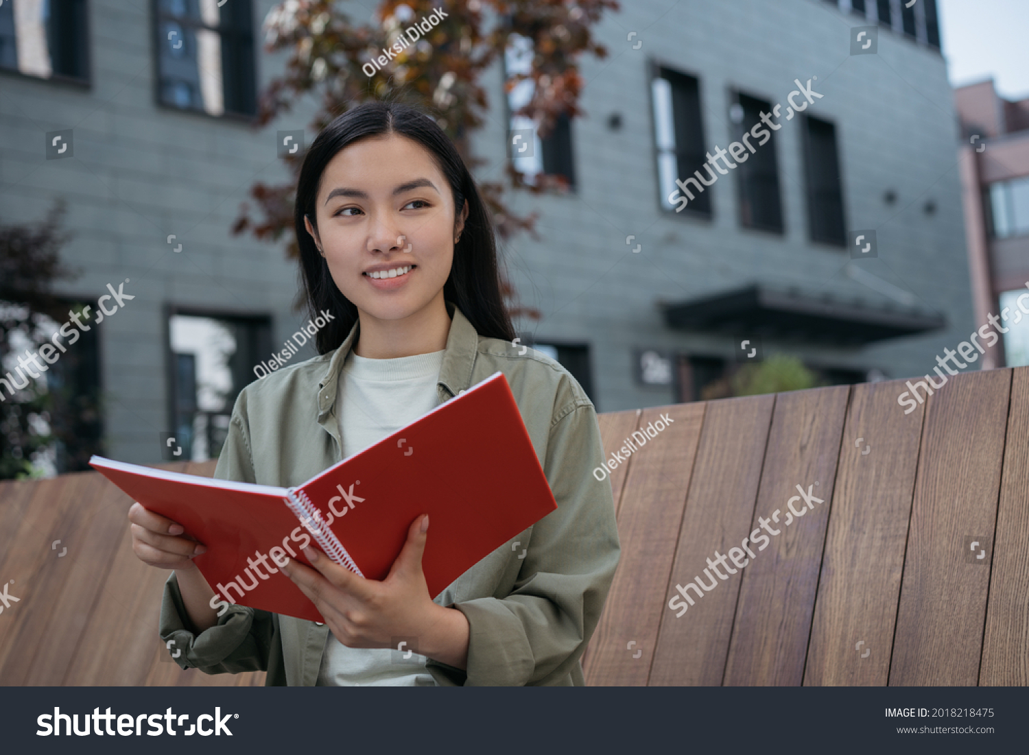 Portrait of pensive asian business woman planning start up project sitting on bench looking away. Smiling student studying holding book exam preparation in university campus. Education concept