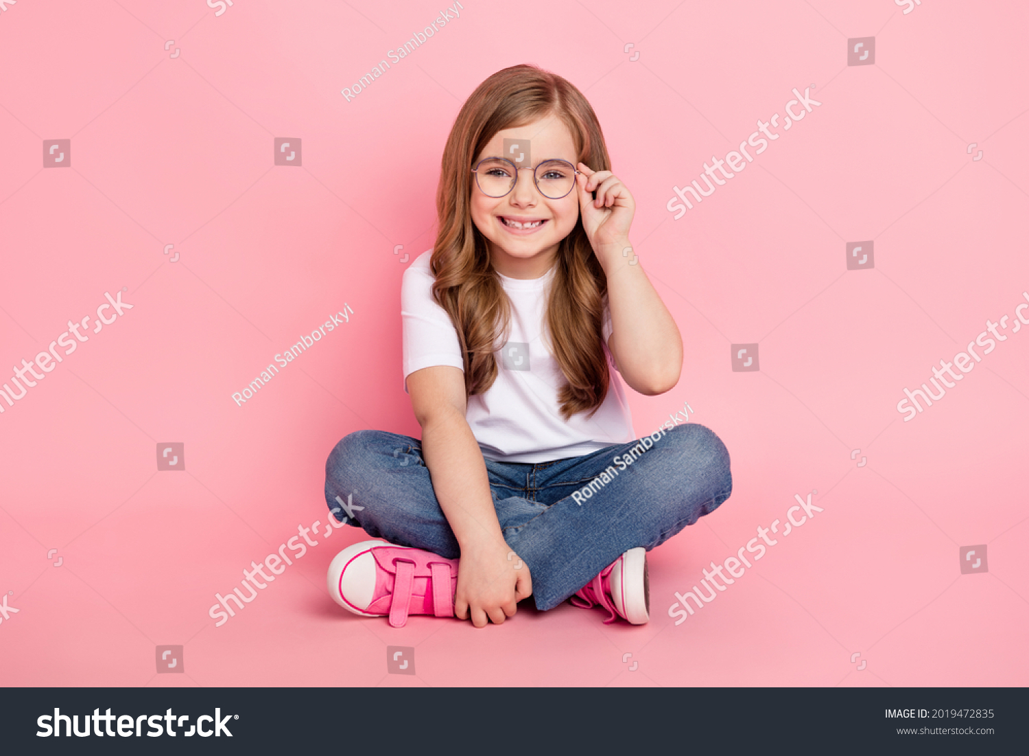 Photo of dream funny little girl sit floor wear glasses white t-shirt jeans shoes isolated pink color background