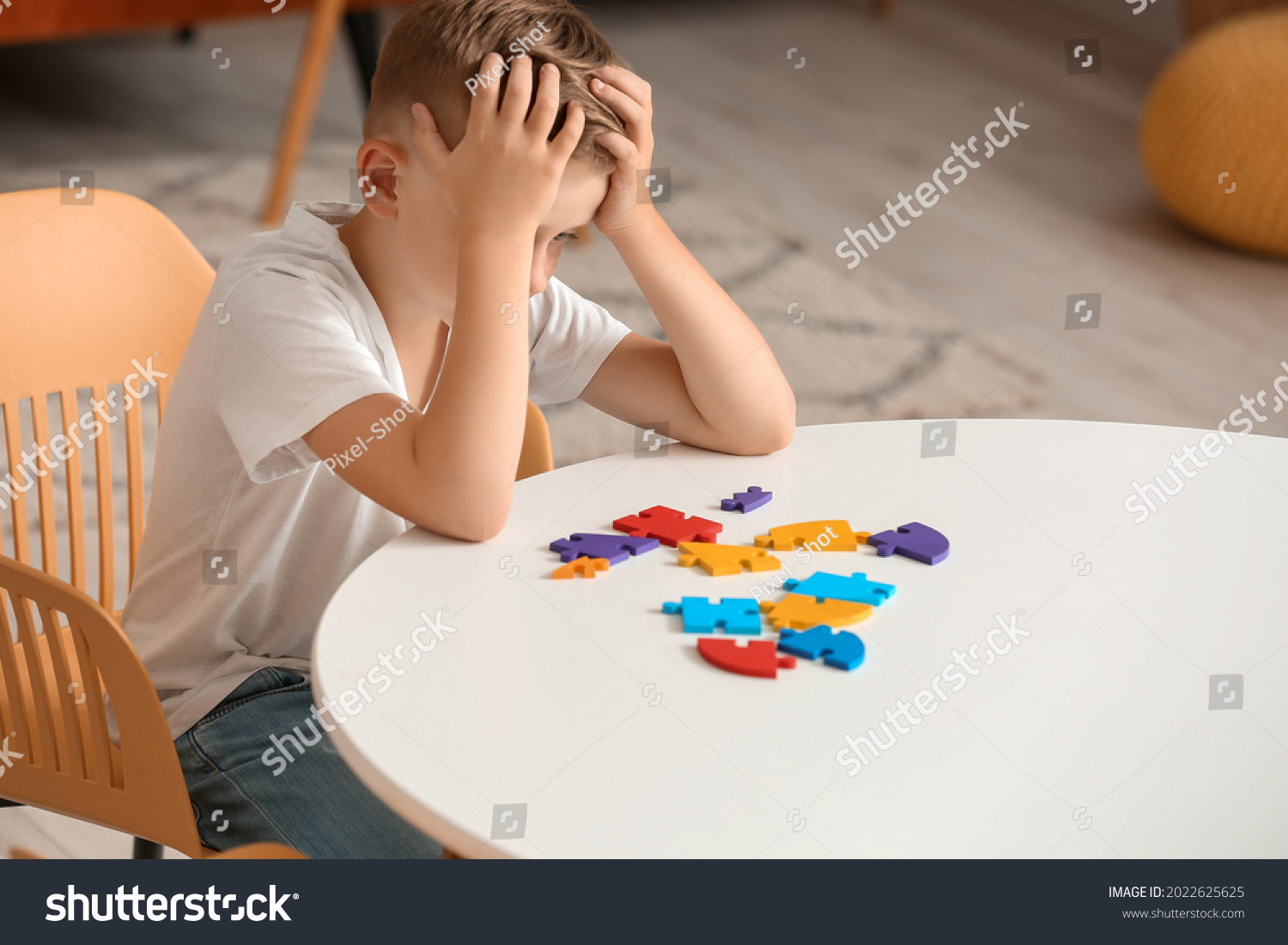 Sad little boy with autistic disorder doing puzzle at home