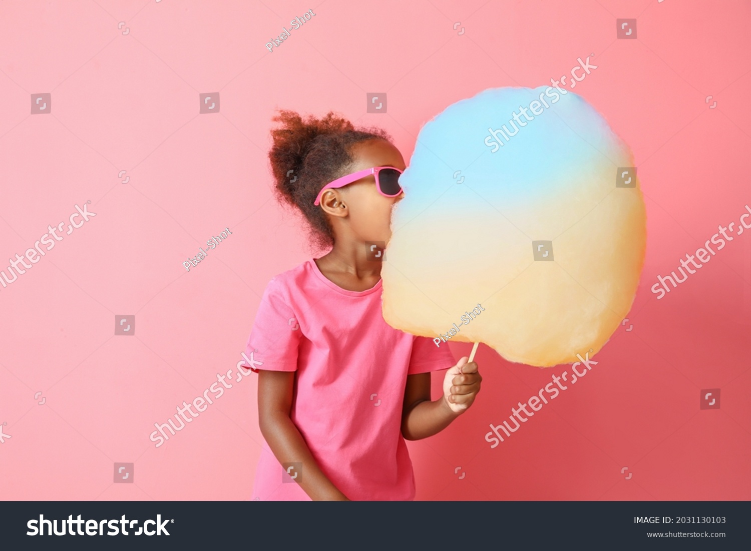 Little African-American girl eating cotton candy on color background