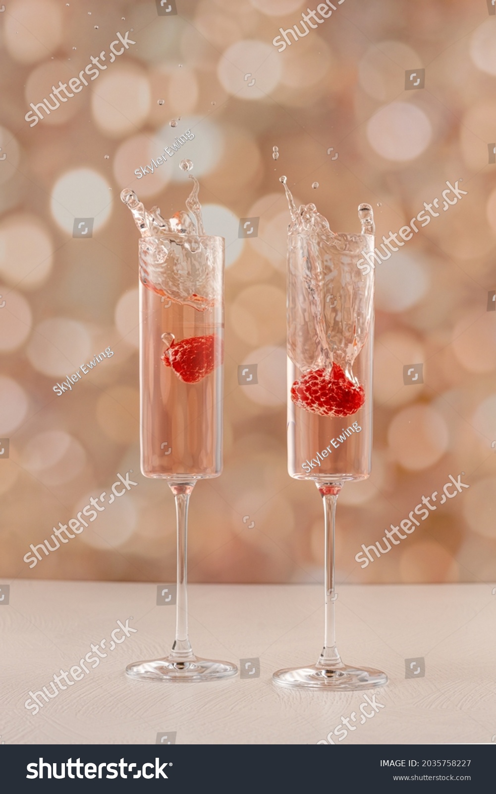 Two champagne glasses splashing with fruit in it. Golden background.