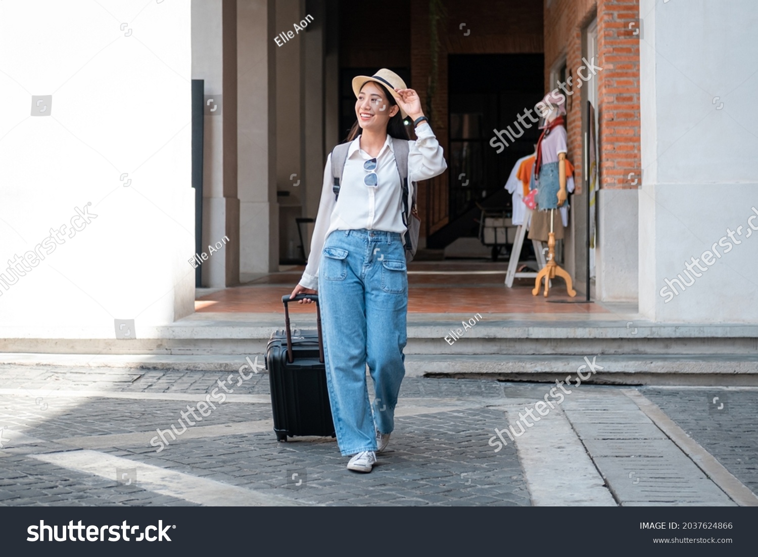 Asian woman tourist is traveling on holiday trip with hat and dragging her black luggage while walking to passengers lounge in the airport