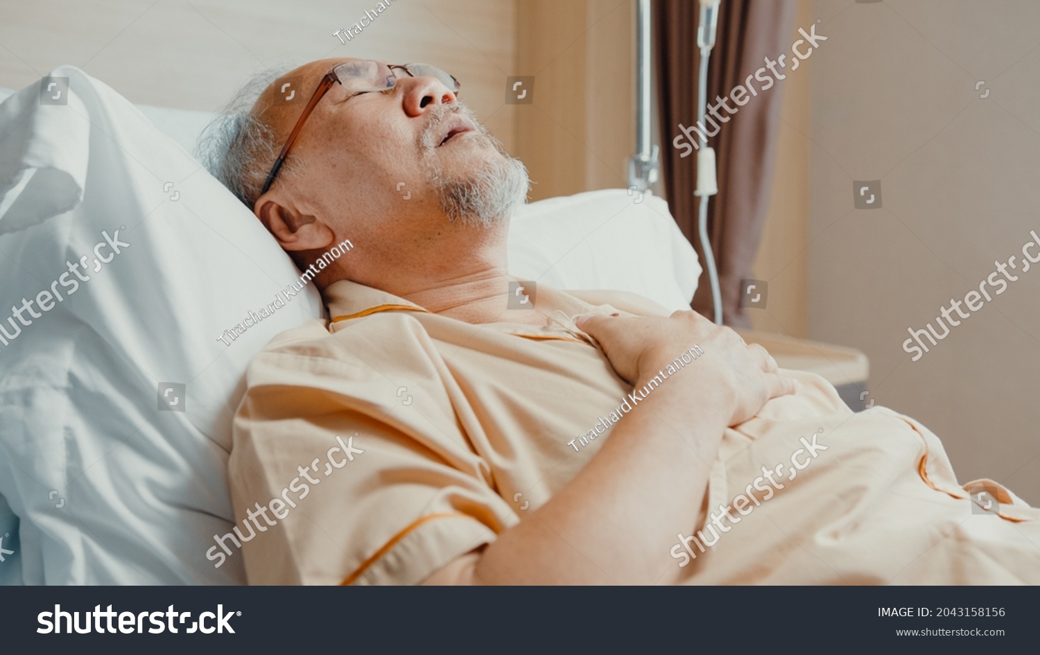 Sad senior Asia man having having heart attack lying on hospital bed and press emergency button. Sick aged guy lying hospitalized in a medical clinic. Health insurance or hospitality concept.