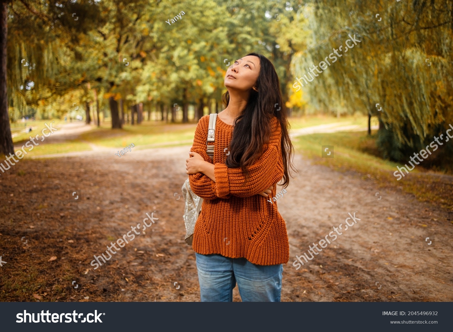 Thoughtful asian woman in autumn park. She looks up.