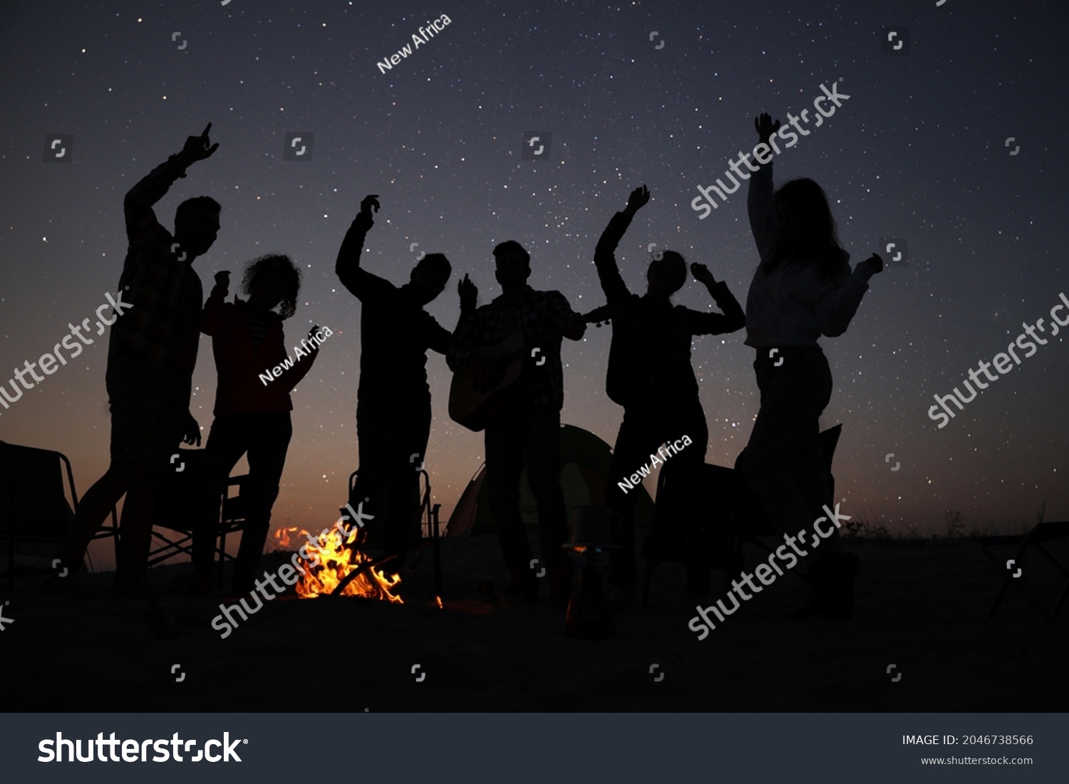 Group of friends having party near bonfire in evening. Camping season