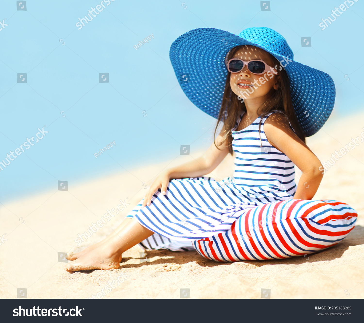 Pretty little girl in a striped dress and hat relaxing on the beach near sea summer vacation travel - concept