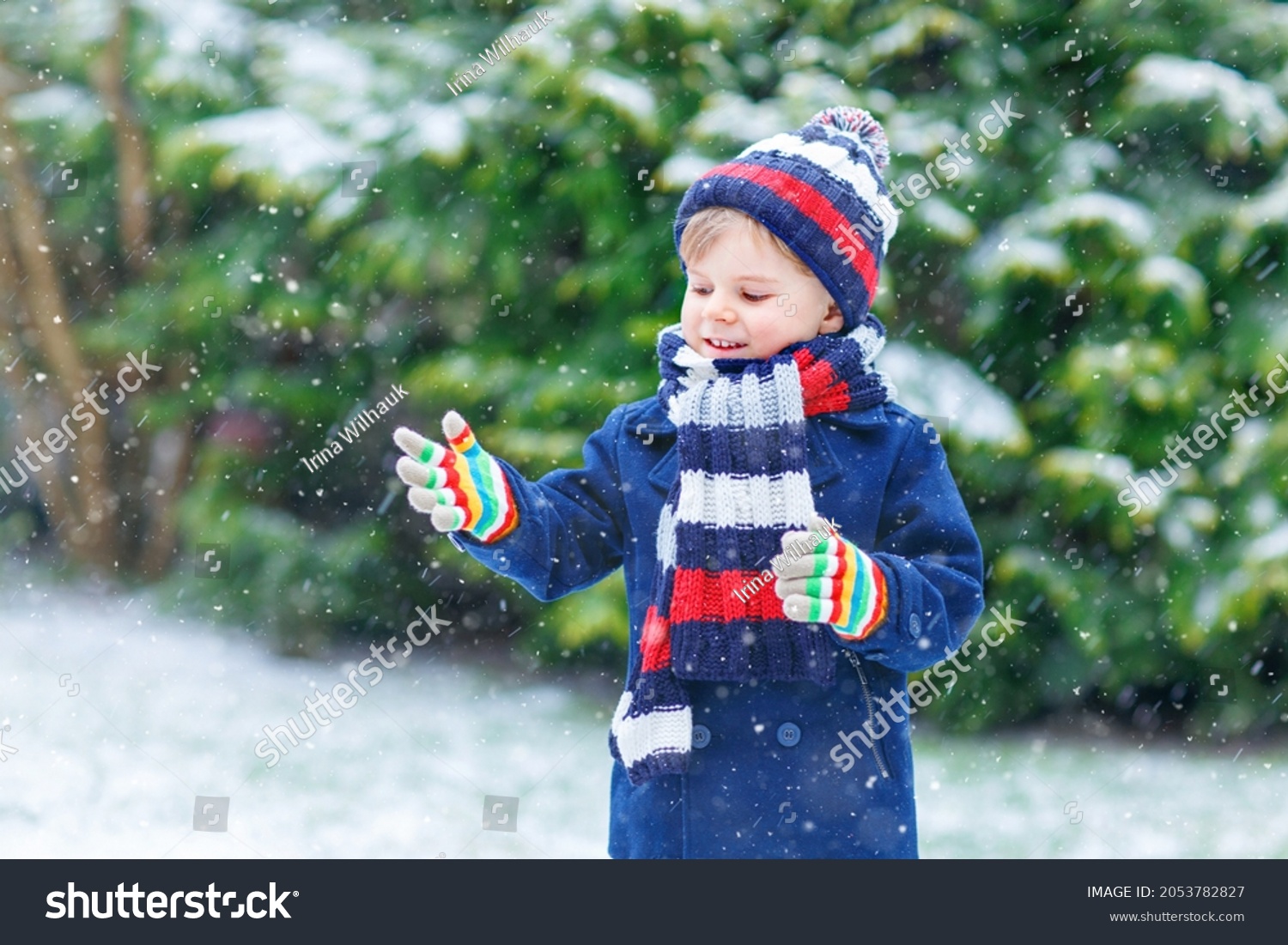 Cute little funny child in colorful winter fashion clothes having fun and playing with snow outdoors during snowfall. Active outdoors leisure with children. Kid boy and toddler catching snowflakes.