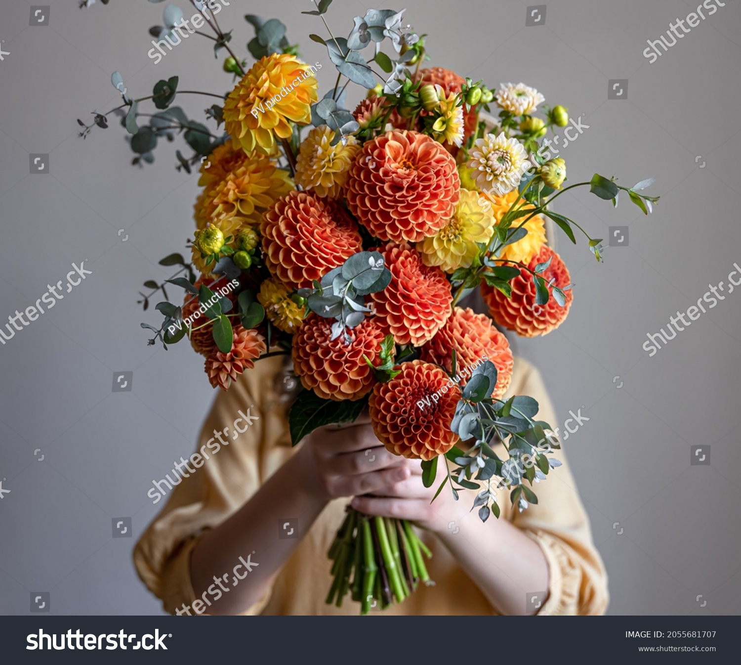 Woman hid her face with a bouquet of yellow and orange chrysanthemums gray background copy space.