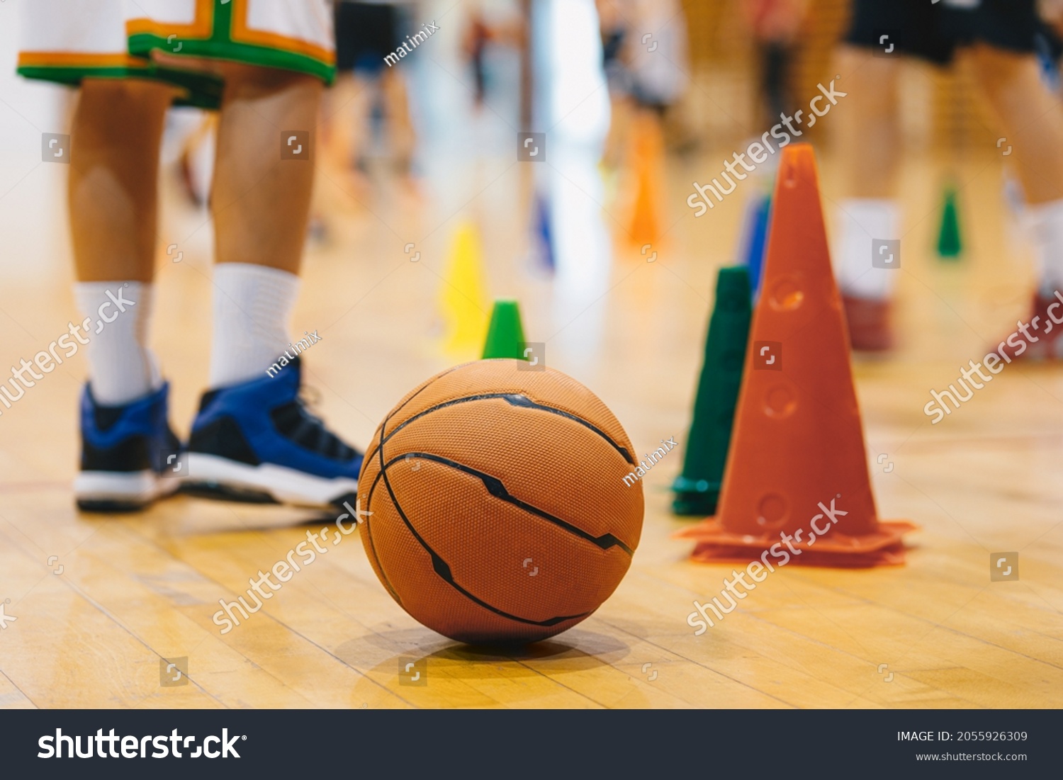 Children Practicing Basketball on School Court. Basketball Training Game Background. Basketball and Training Cones on Wooden Floor Close Up with Blurred Players Playing Basketball Game in Background
