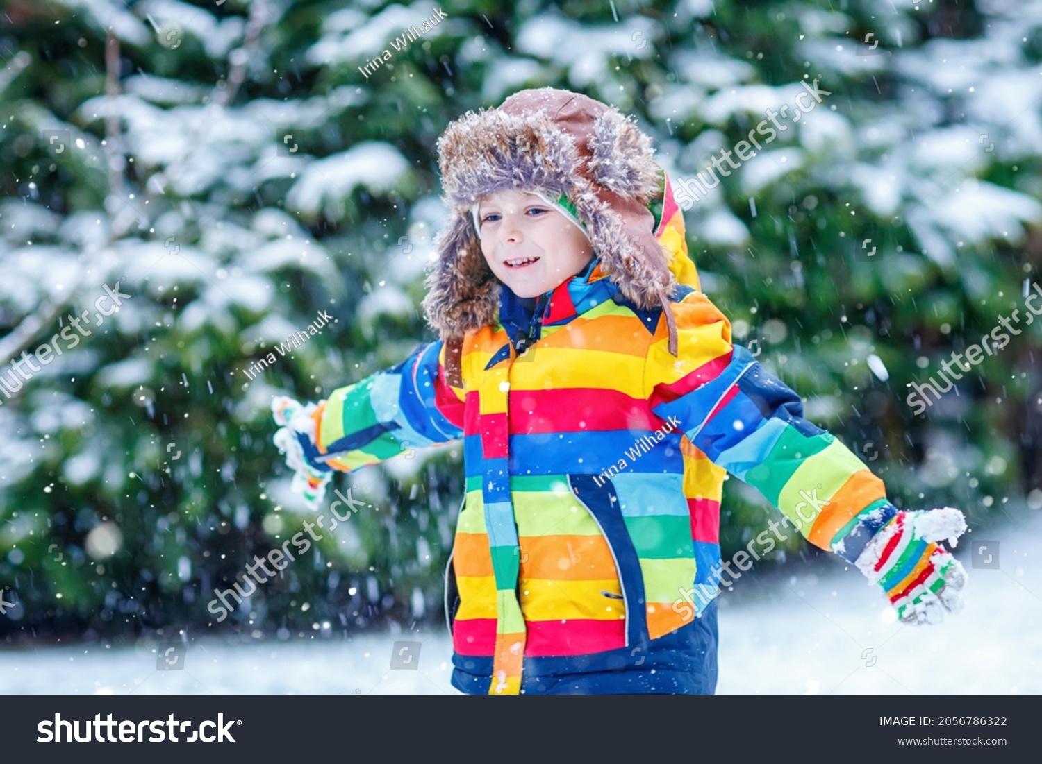 Cute little funny child in colorful winter fashion clothes having fun and playing with snow outdoors during snowfall. Active outdoors leisure with children. Kid boy and toddler catching snowflakes