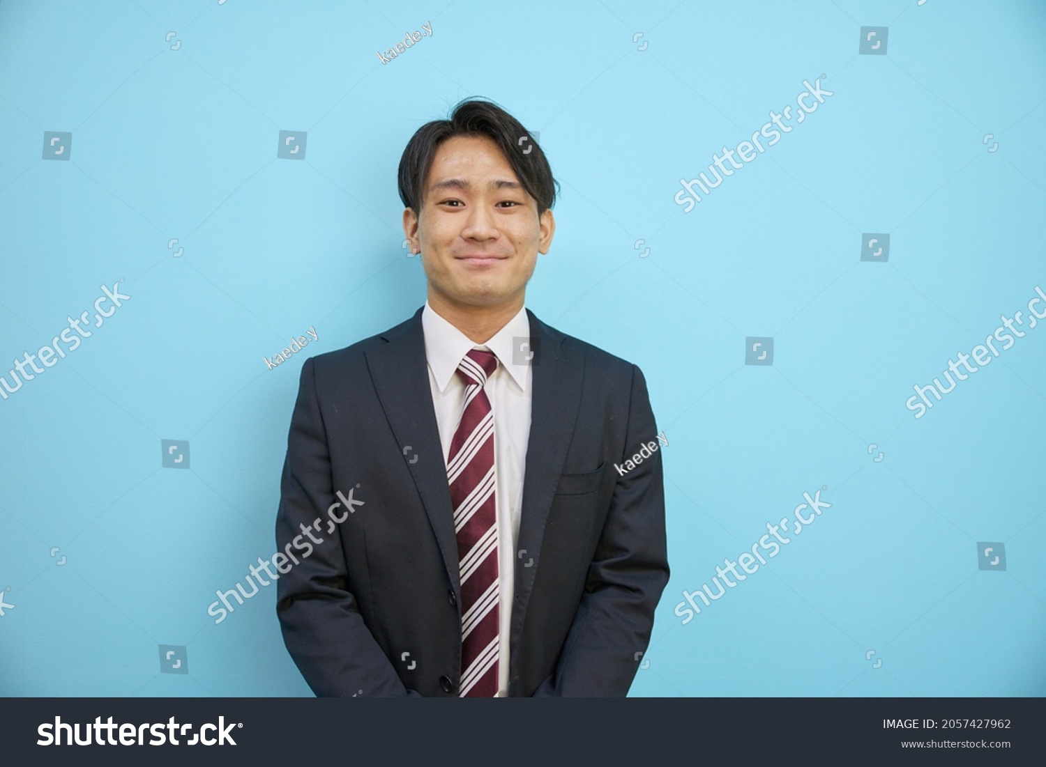 Japanese man in a suit laughing refreshingly in front of a blue background