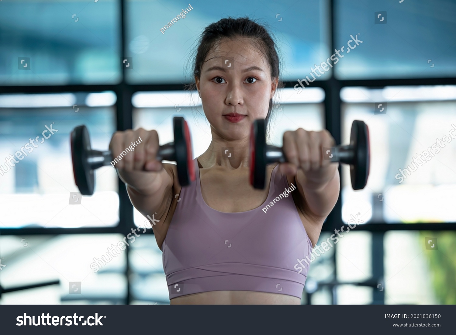 Close up an asian woman raises a pair of dumbbells in front of her to build arm muscles