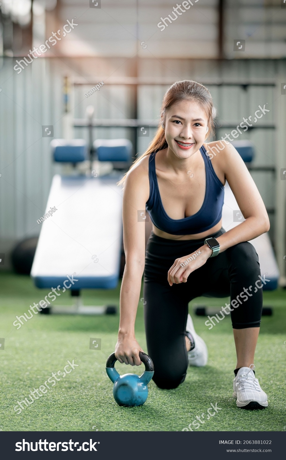Beautiful asian sport woman sitting on the floor with kettle ball at gym. Smiling and looking at camera. Vertical view.