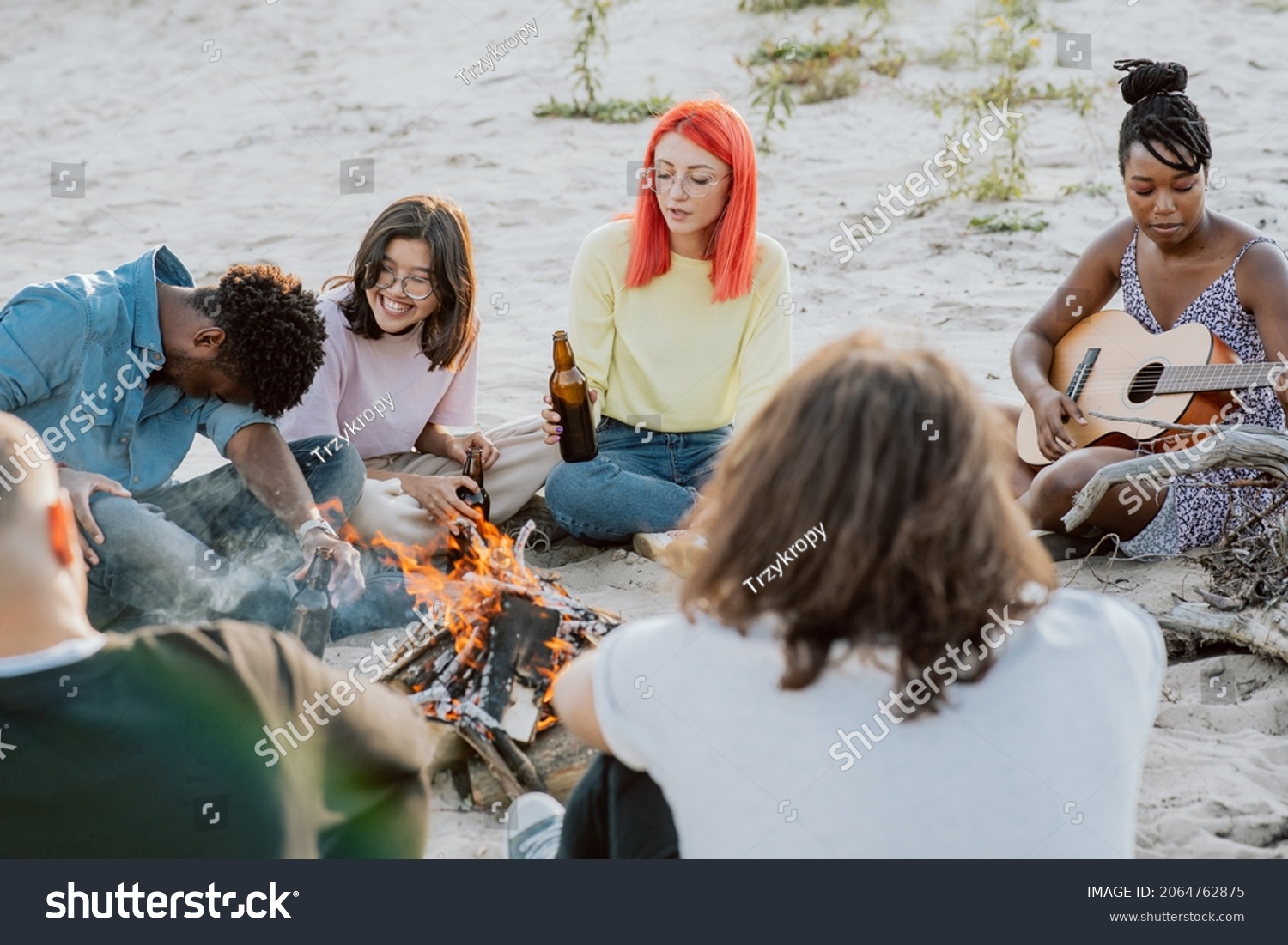 Bonfire of friends in open air  outside  dark-skinned beautiful girl plays guitar  rest of people listen  drink beer  joke around  fool around  talk  good atmosphere  time off from school  work