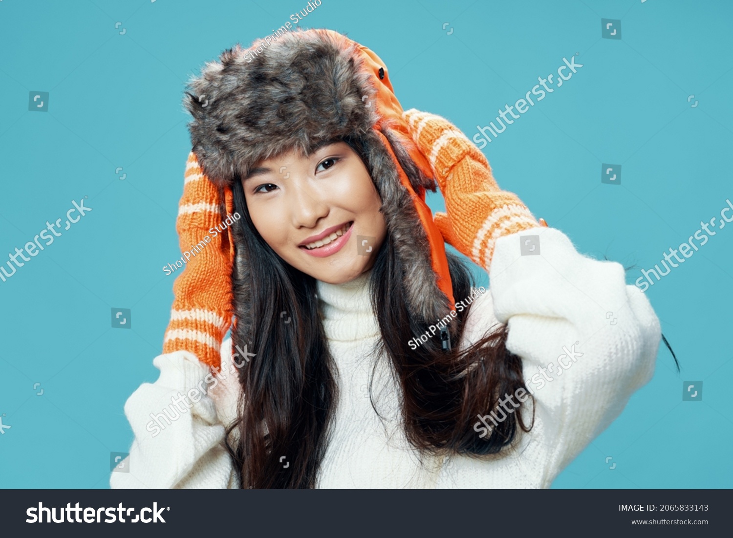happy woman in gloves holding cap on her head on blue background cropped view