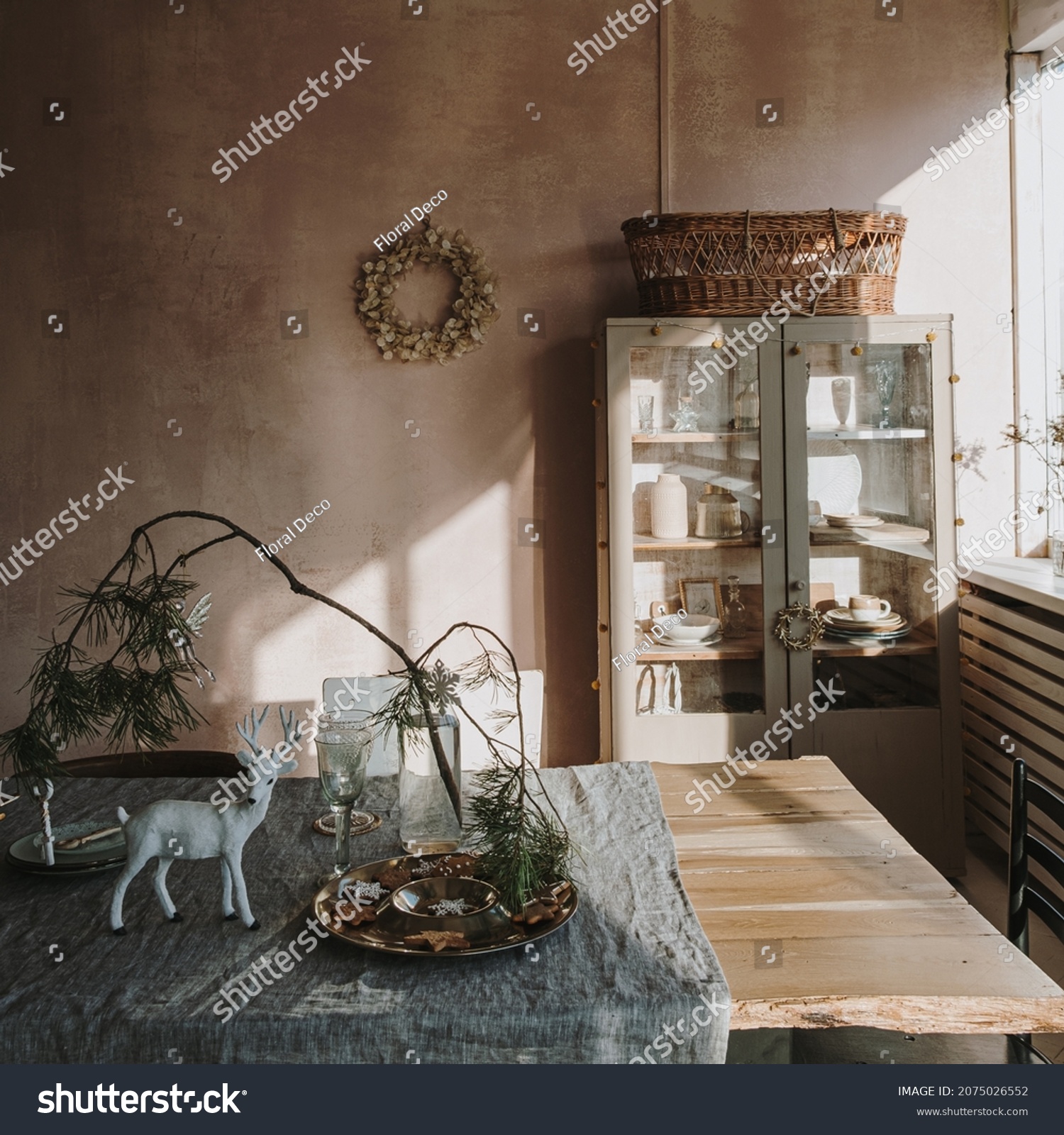 Elegant aesthetic home living or dinning room interior design with dinner table  linen table cloth  fir branch bouquet  Christmas wreath  neutral dusty pink walls. Sunlight shadows on the wall