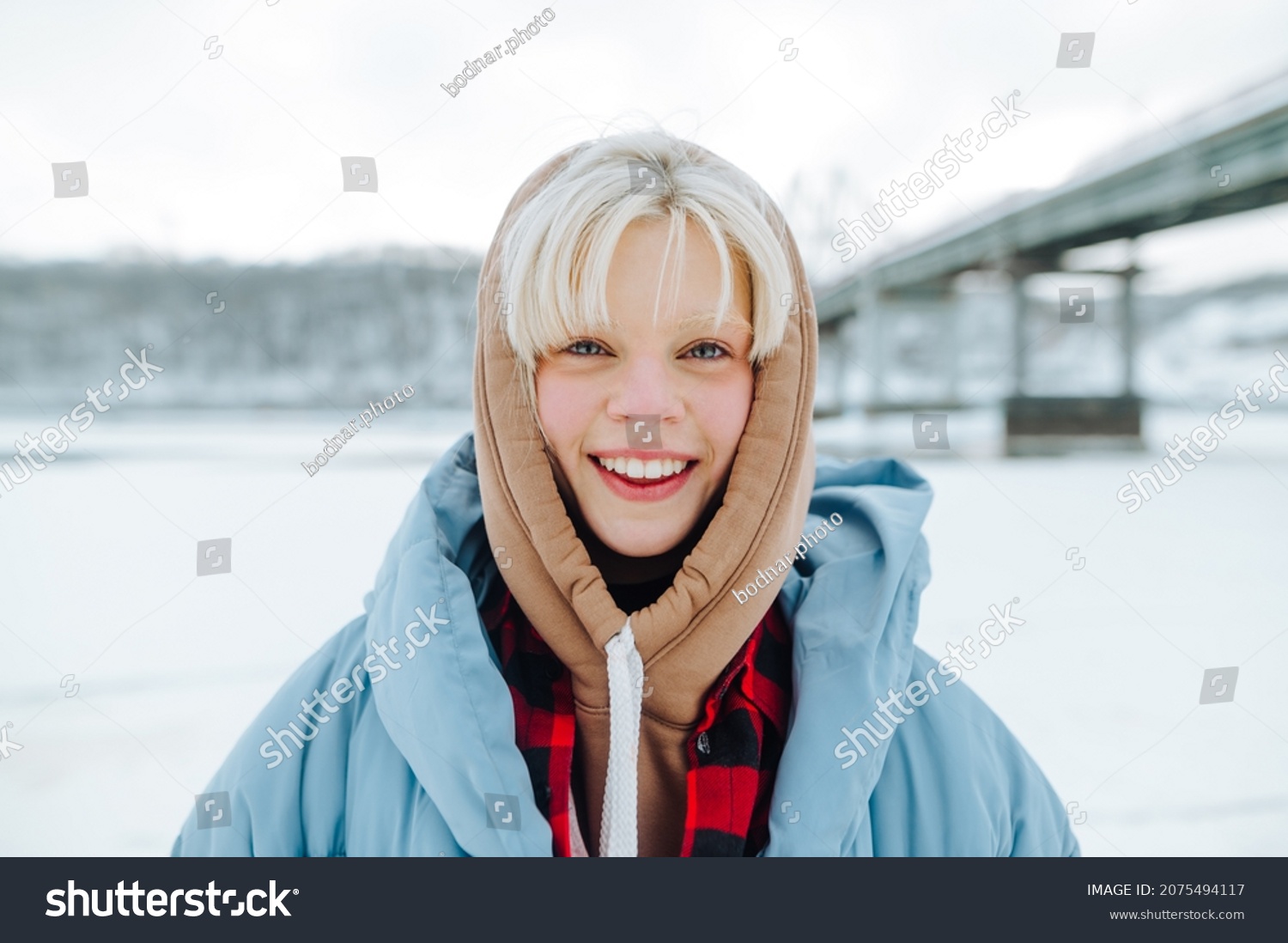 Portrait of a positive girl on a winter walk on the street on a background of snowy landscapes  looking at the camera with a smile on his face