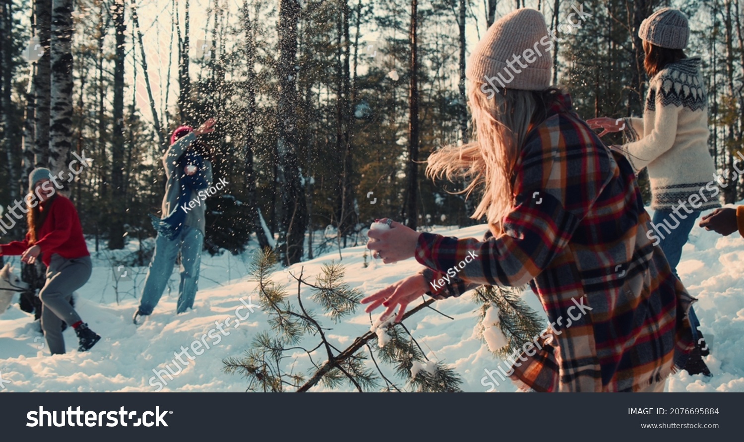 Idyllic cinematic shot  happy diverse friends enjoying fun snowball fight at snowy winter forest with dog slow motion.