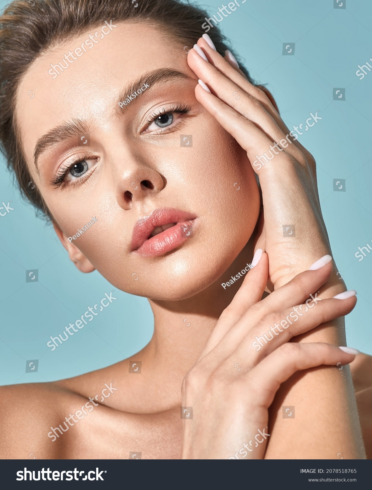 Skin care. Beautiful woman with healthy facial skin touching her moisturized face skin on blue background. High quality