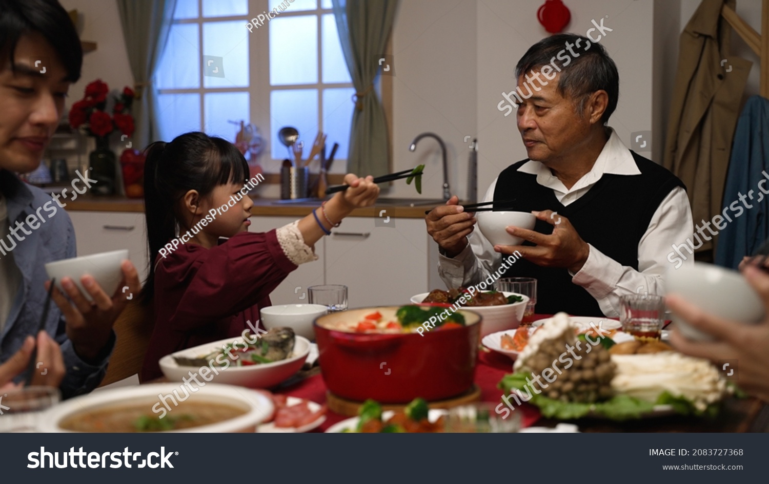 happy asian grandfather talking with hand gestures as his polite granddaughter putting food into his bowl at dinner table on chinese new year's eve at home