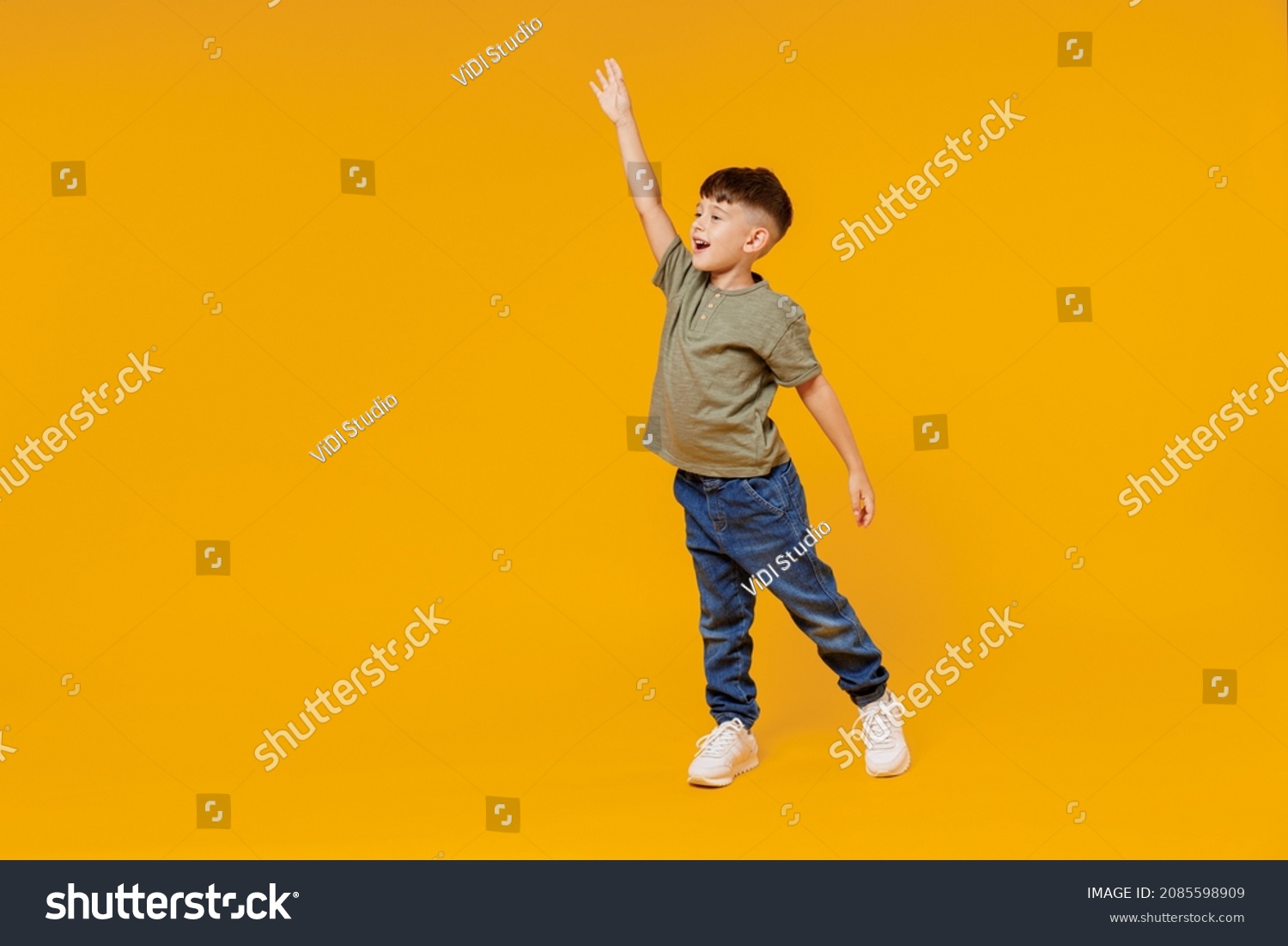 Full body side view little small smiling happy boy 6-7 years old wear green t-shirt walk go waving hand isolated on plain yellow background studio portrait. Mother's Day love family lifestyle concept