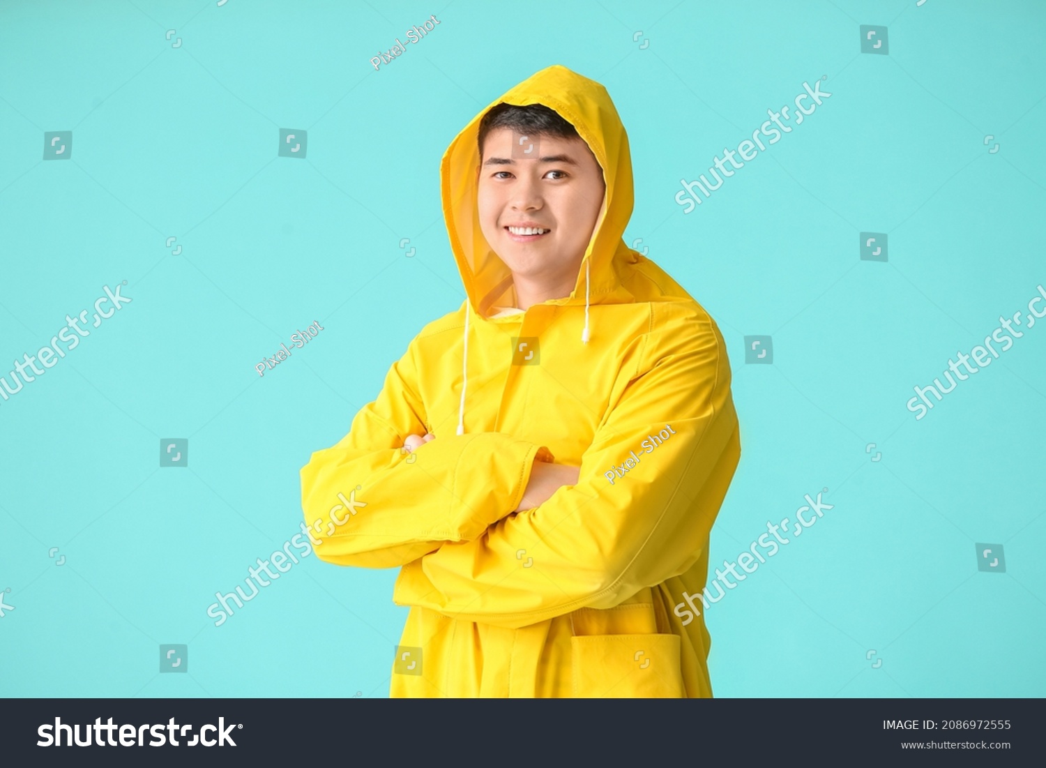 Young Asian man in raincoat on color background