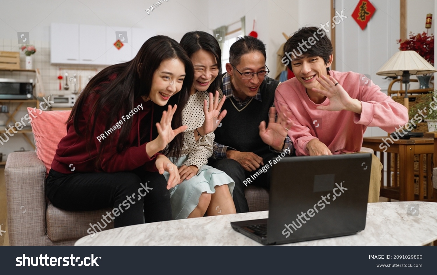 asian family of four waving hi and wishing friend happy chinese lunar new year with congratulation hand gestures through video chat on computer in the living room. text on door translation: spring