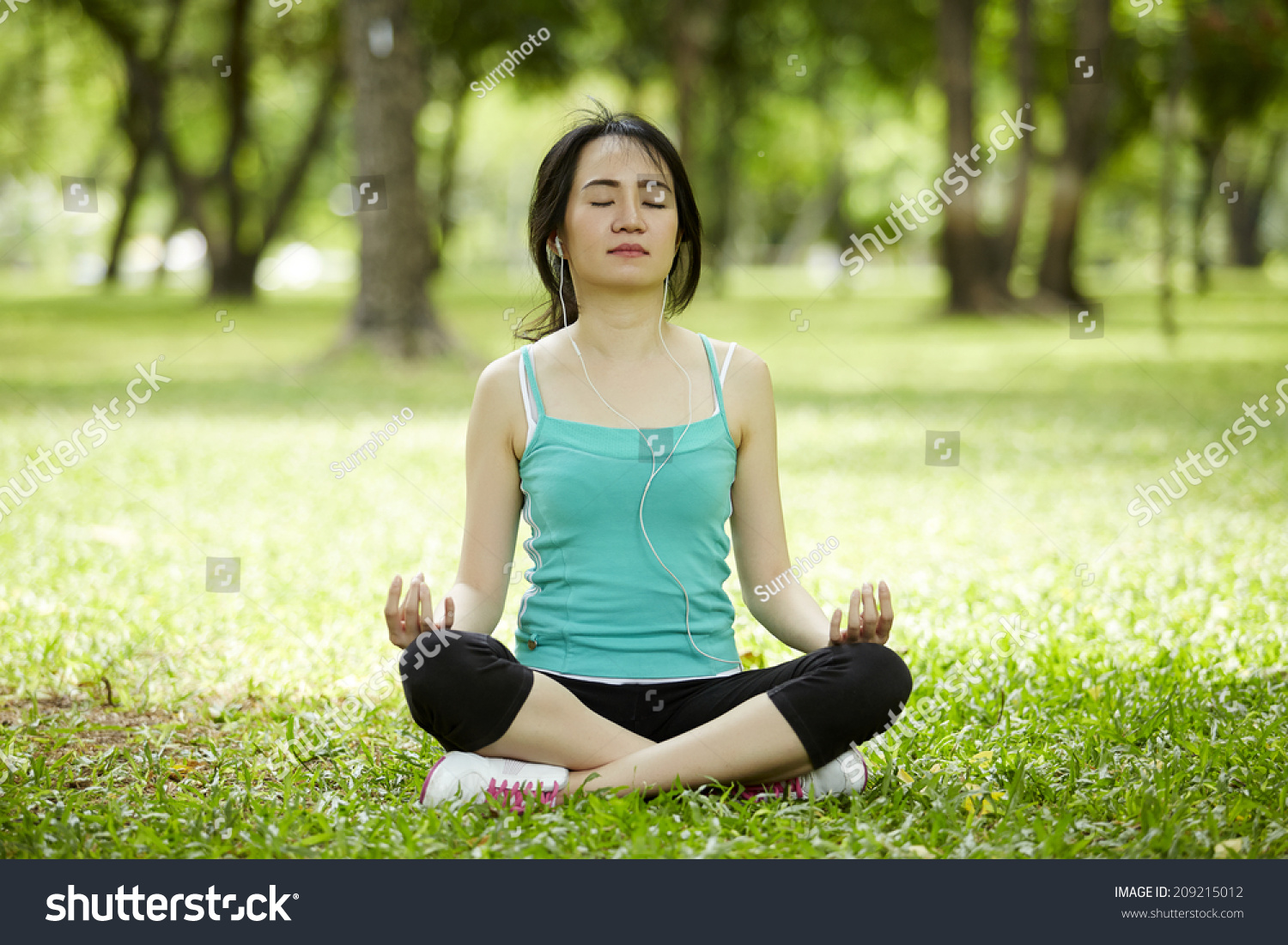 a beautiful woman with earbuds doing yoga meditation outdoor in