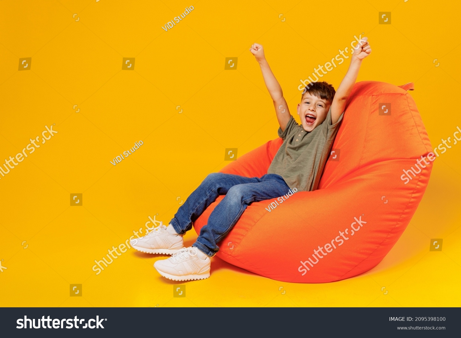 Full body little small smiling happy boy 6-7 years old wearing green t-shirt sit in bag chair stretch hands shout isolated on plain yellow background studio Mother's Day love family lifestyle concept