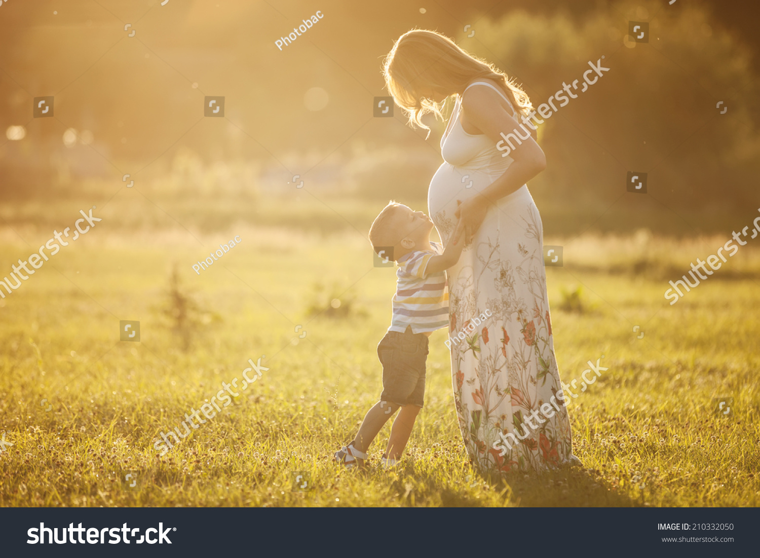 Small boy kissing belly of his pregnant mother outdoors