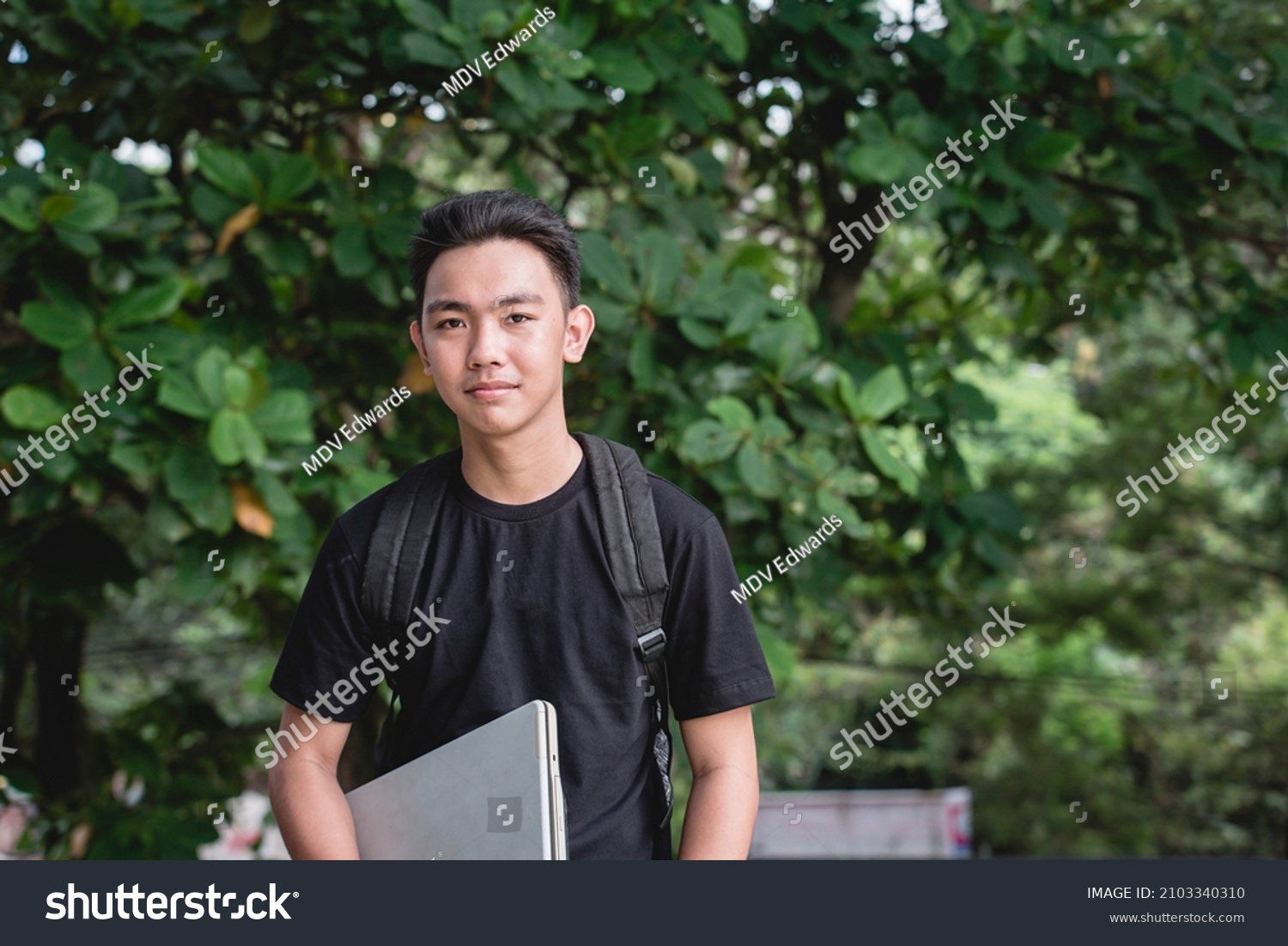 A young college student with a backpack and carrying his laptop while outside the school campus.