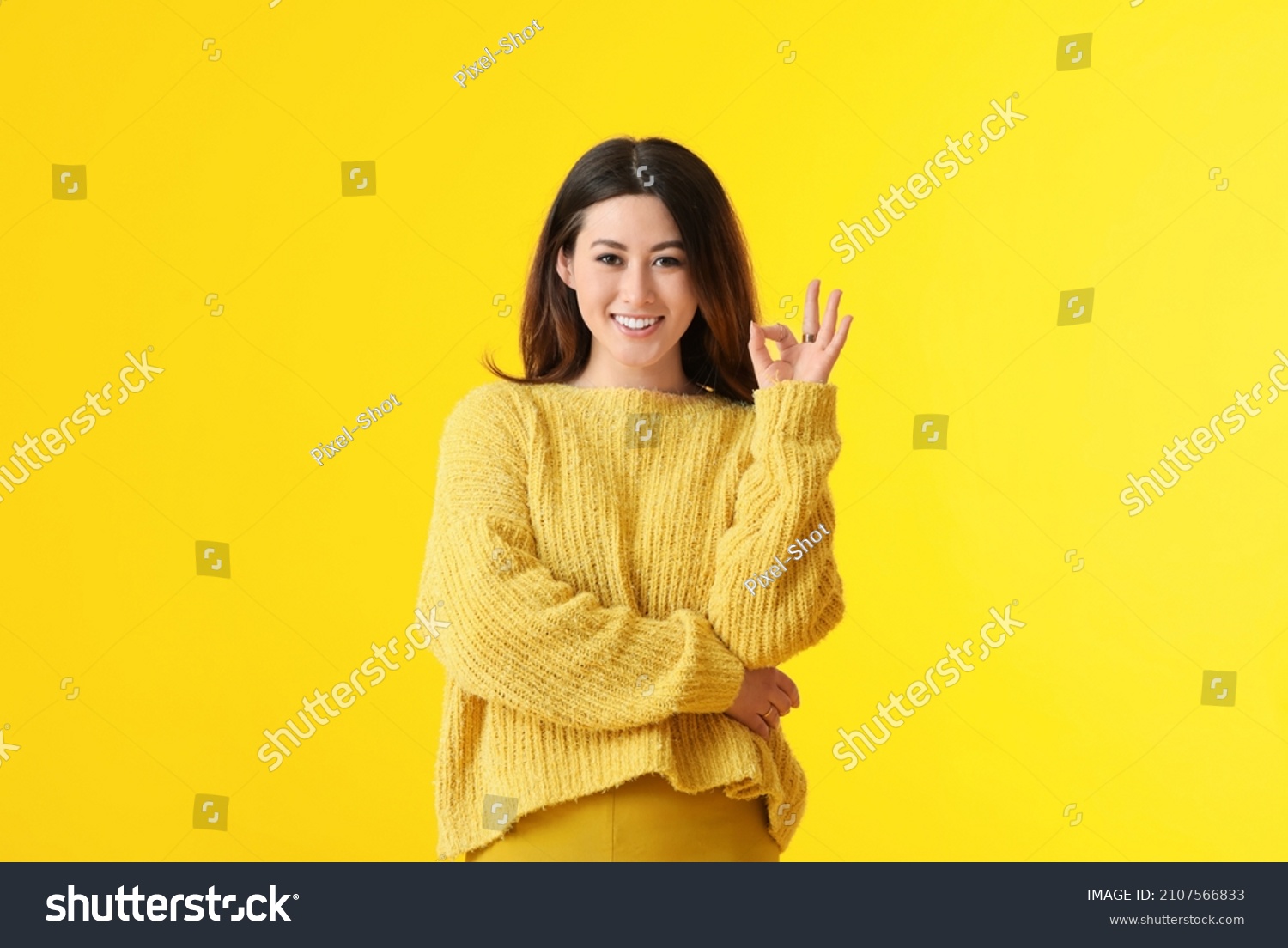 Beautiful young Asian woman showing OK on yellow background