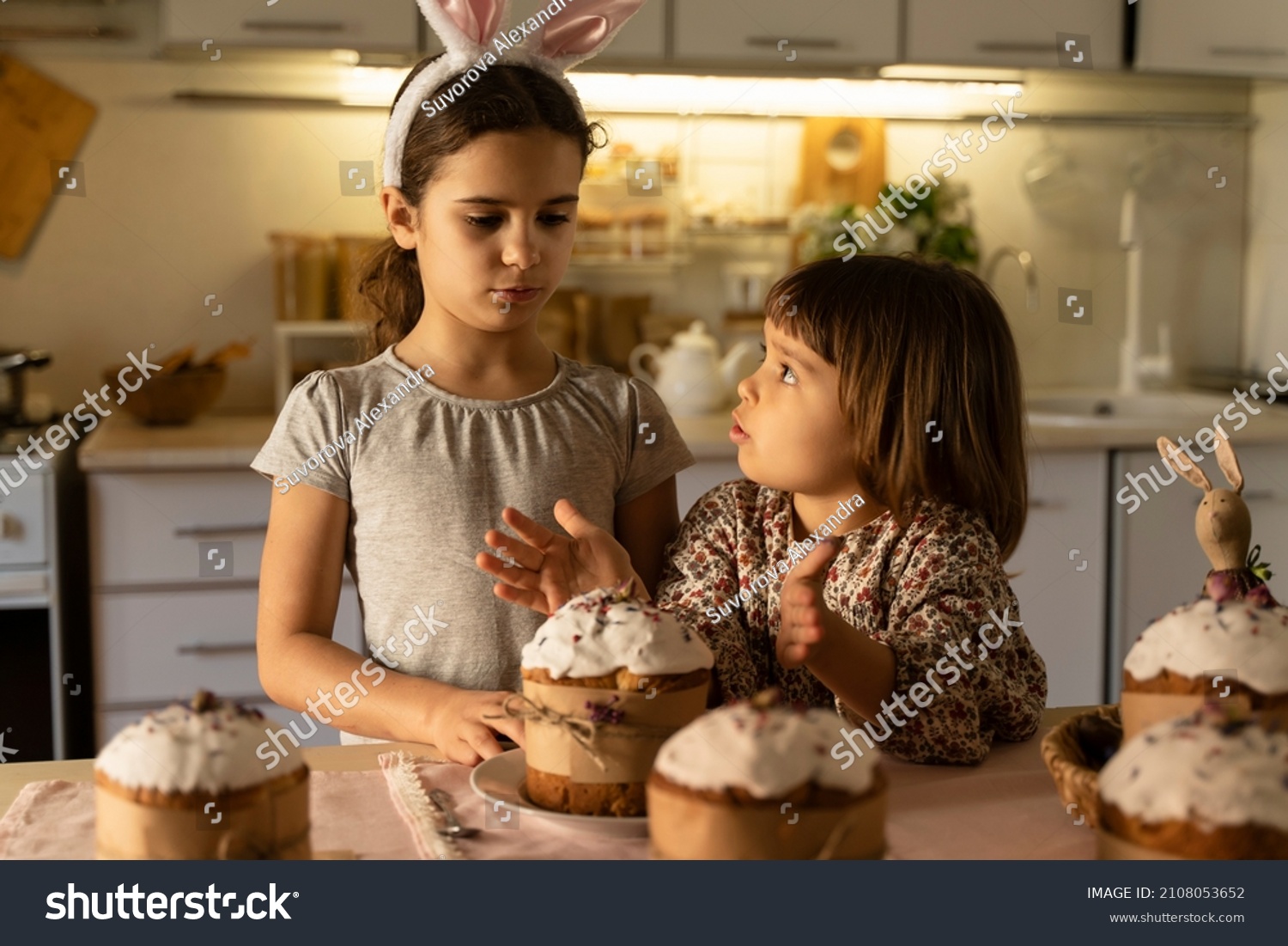 Cute little sisters want to eat Easter cake at home in the kitchen on the eve of the holiday. Happy Easter. Children decorate the house for Easter lifestyle sisters relationships in the family