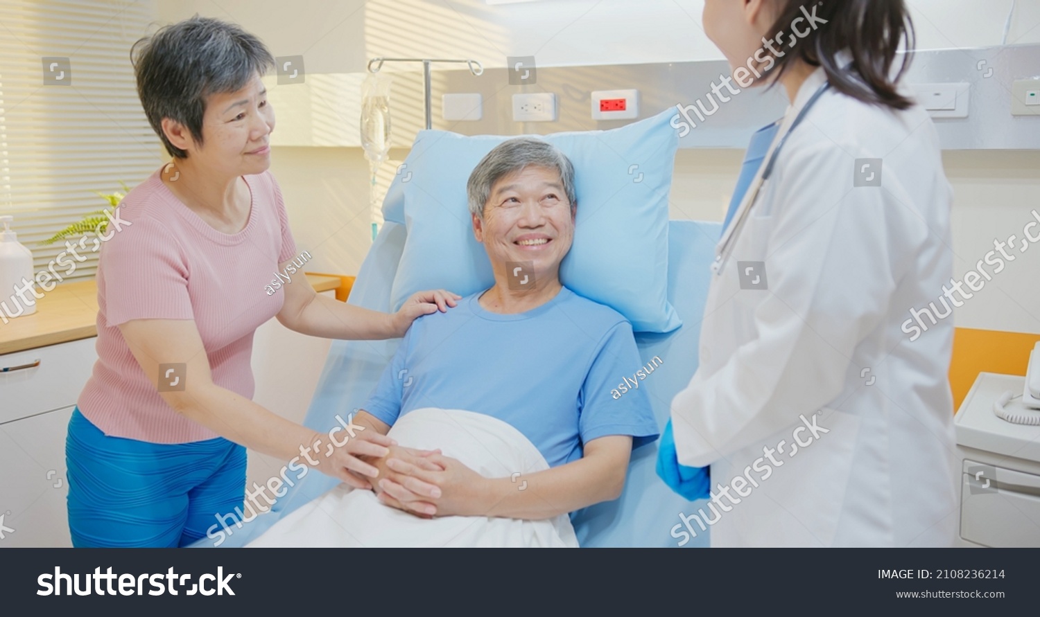 Senior people healthcare concept - asian female doctor is talking to senior man patient lying in bed while elder woman take care of him at hospital