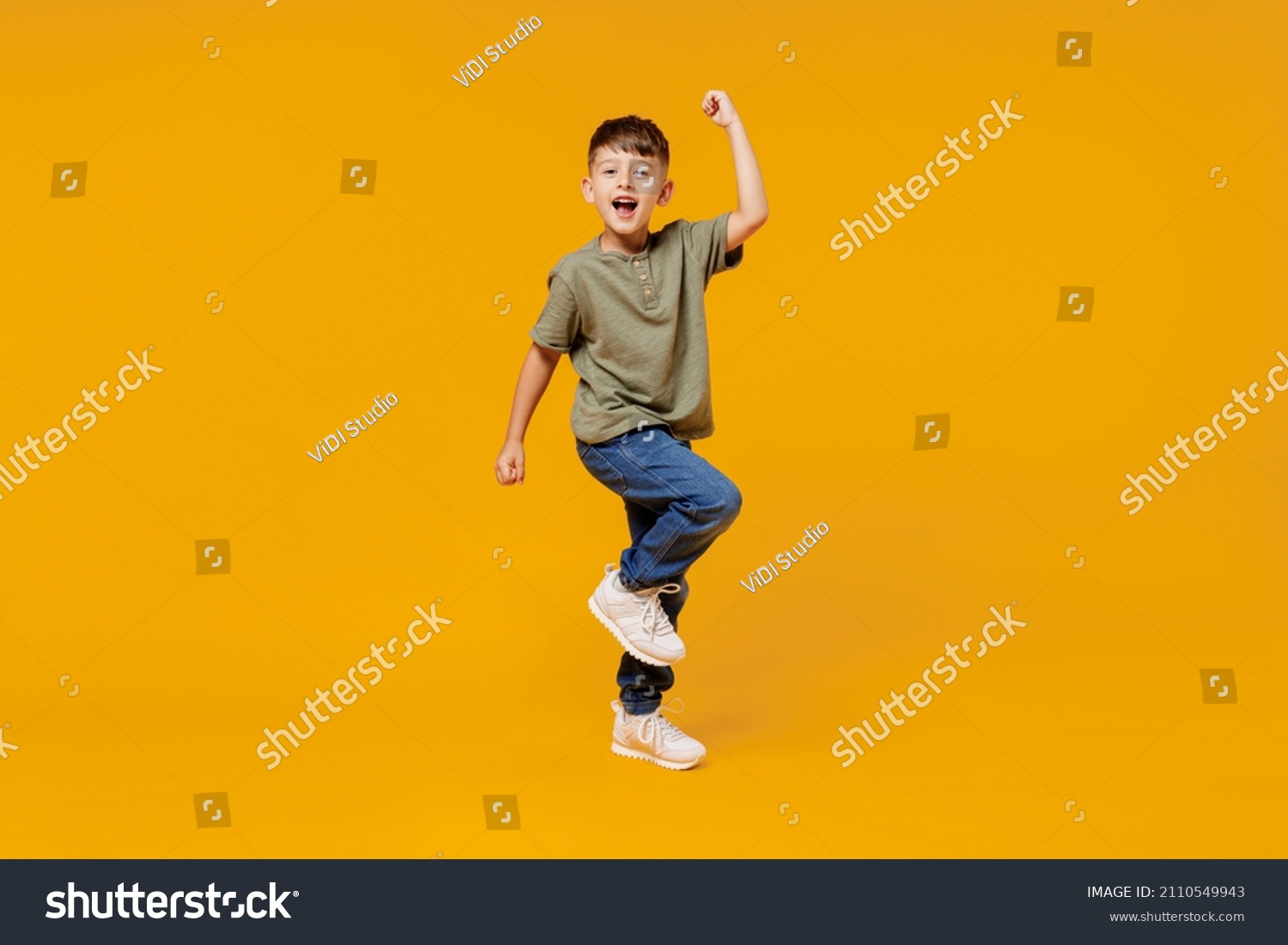 Full body little small fun happy boy 6-7 years old wearing green t-shirt do winner gesture clench fist isolated on plain yellow background studio portrait. Mother's Day love family lifestyle concept